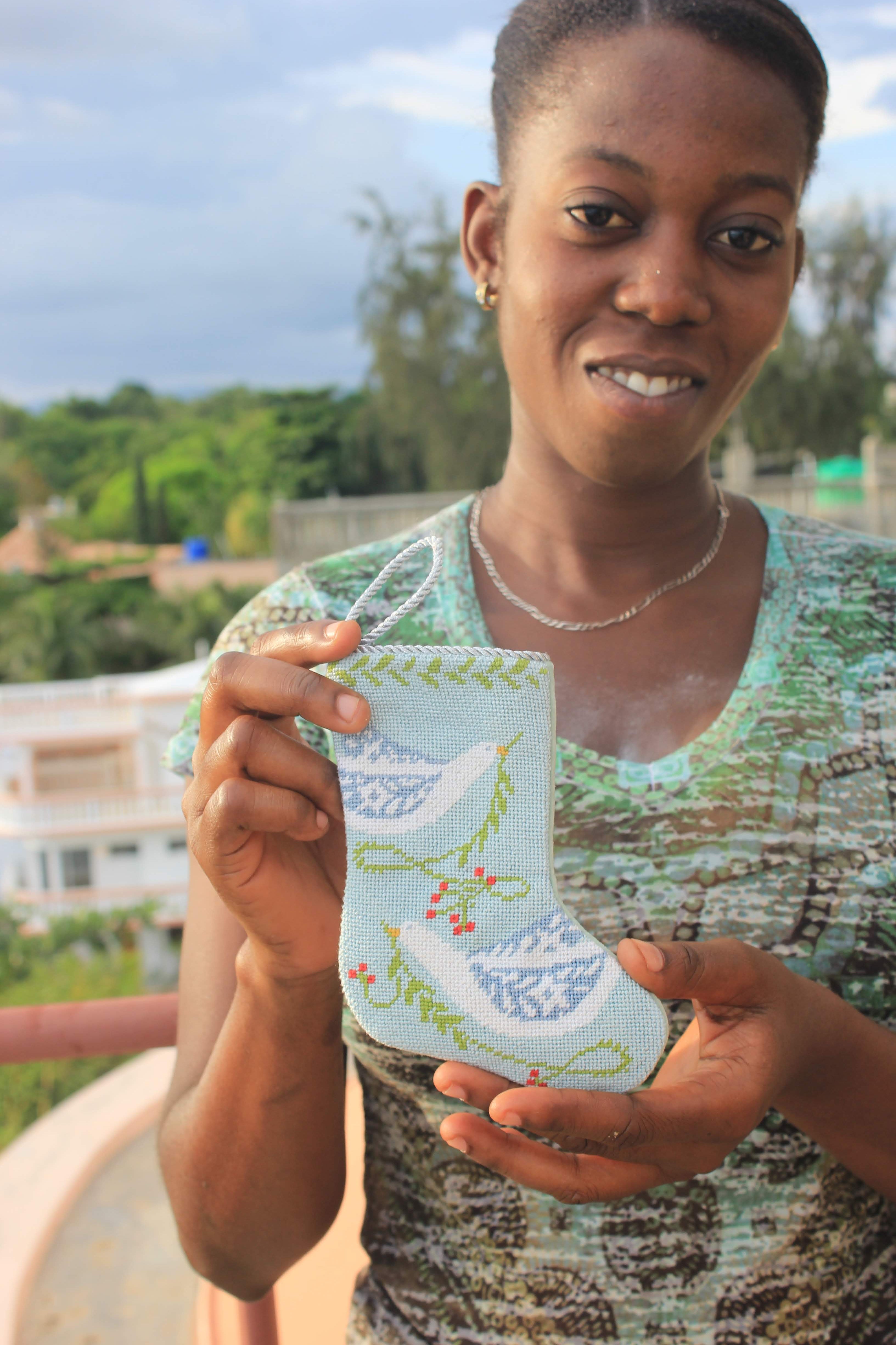 Haitian woman holding a mini stocking ornament with light blue and green bird design