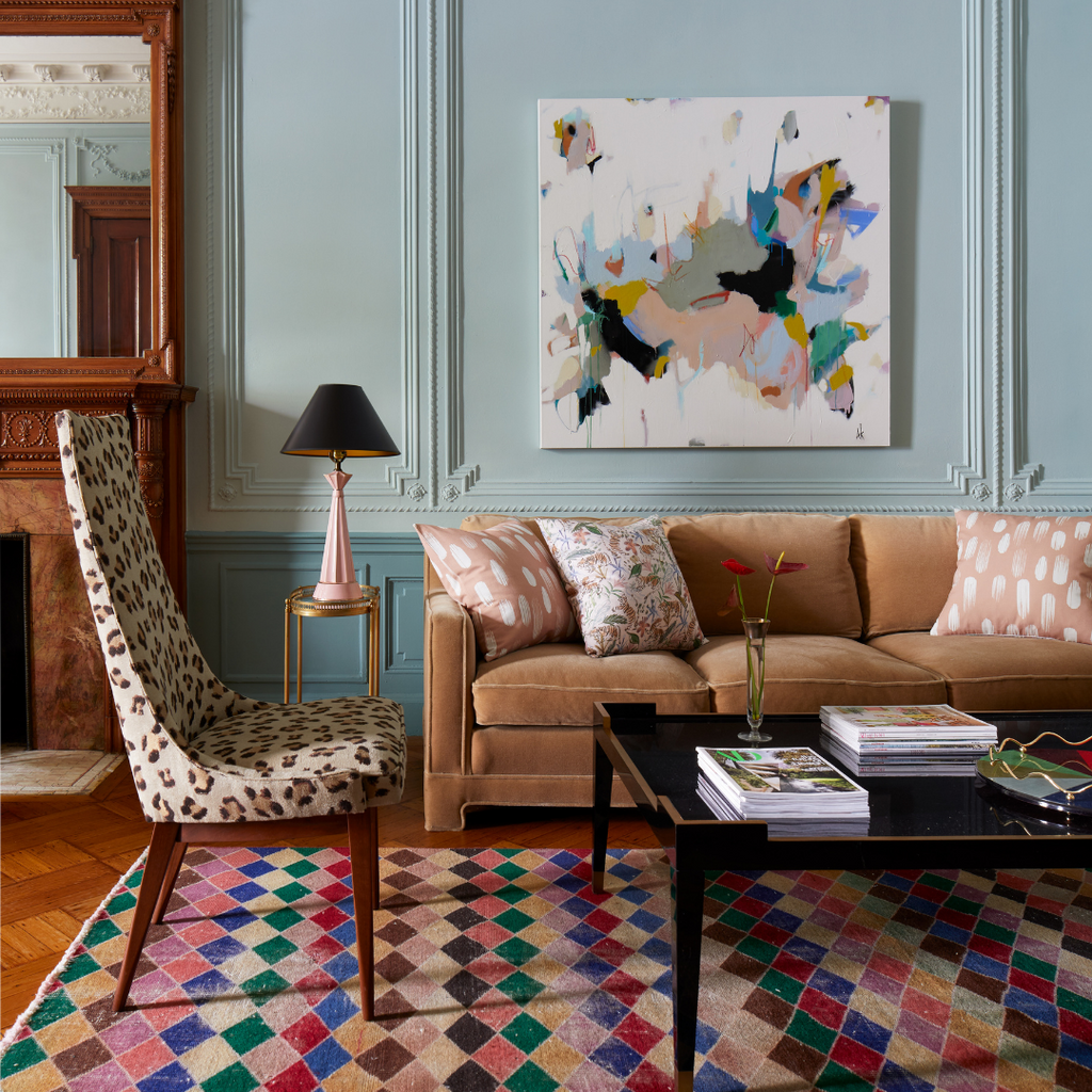 Living room with a cheetah printed chair and an apricot orange couch styled with a pink and white pillow and a Pink Chinoiserie Tiger Custom Pillow over a black coffee table and an artwork hung on a baby blue wall