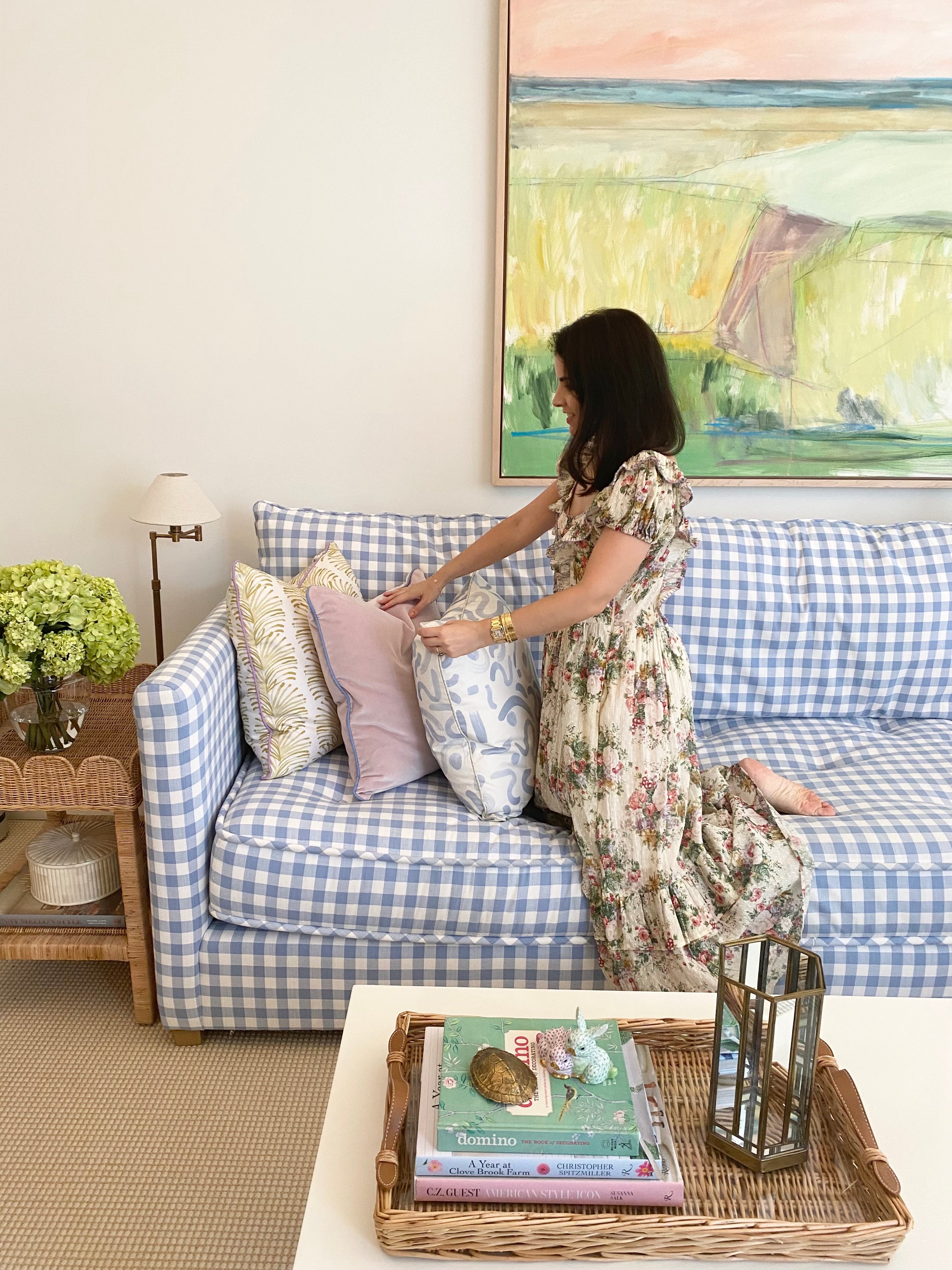 Living room styled with Yellow Stripe Chartreuse custom pillow, pink velvet custom pillow, and sky blue custom pillow on blue and white couch next to brunette woman wearing a cream floral dress next to white coffee table with books and decorations