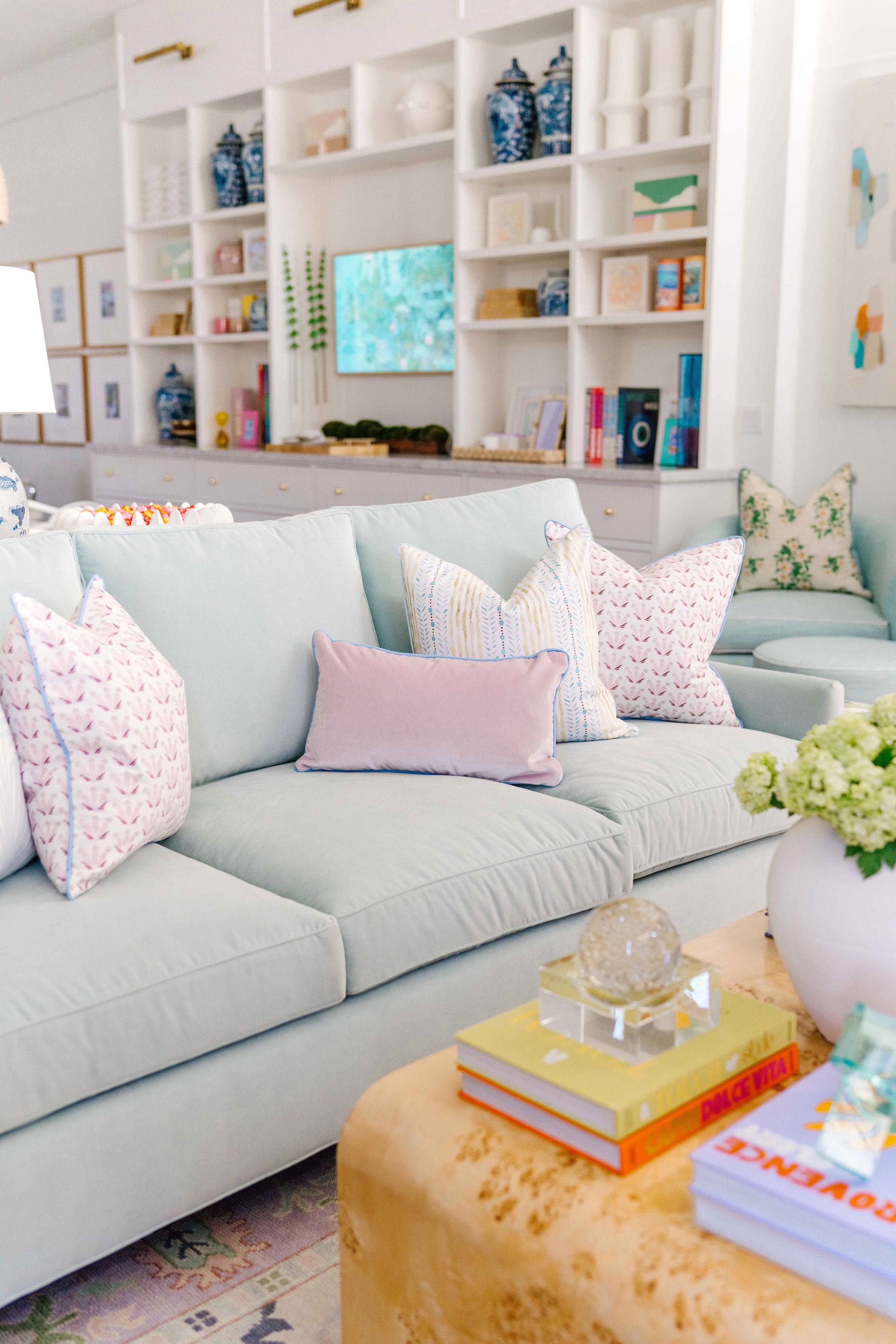 Living room styled with a blue green velvet couch with a Sky Blue Botanical Stripe custom pillow, a Pink & Burgundy Drop Repeat Floral, a Blue & Green Striped custom pillow, and a pink velvet custom lumbar pillow in front of a coffee table