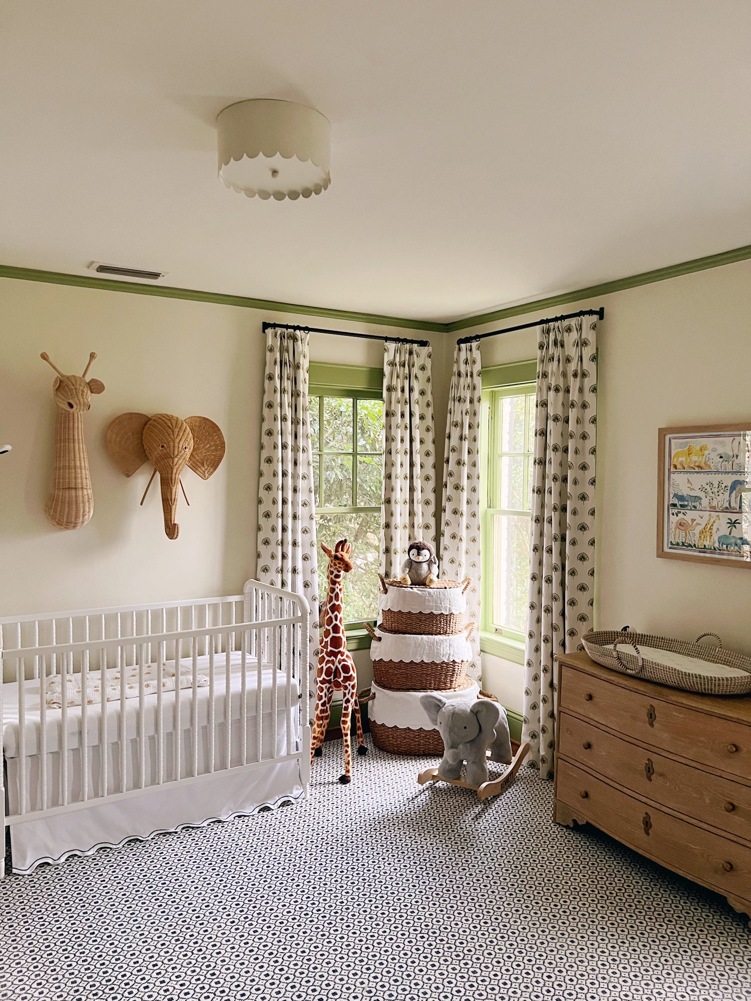 Green floral custom curtains hanging on a rod in a green painted nursery styled with a white crib and rattan animals