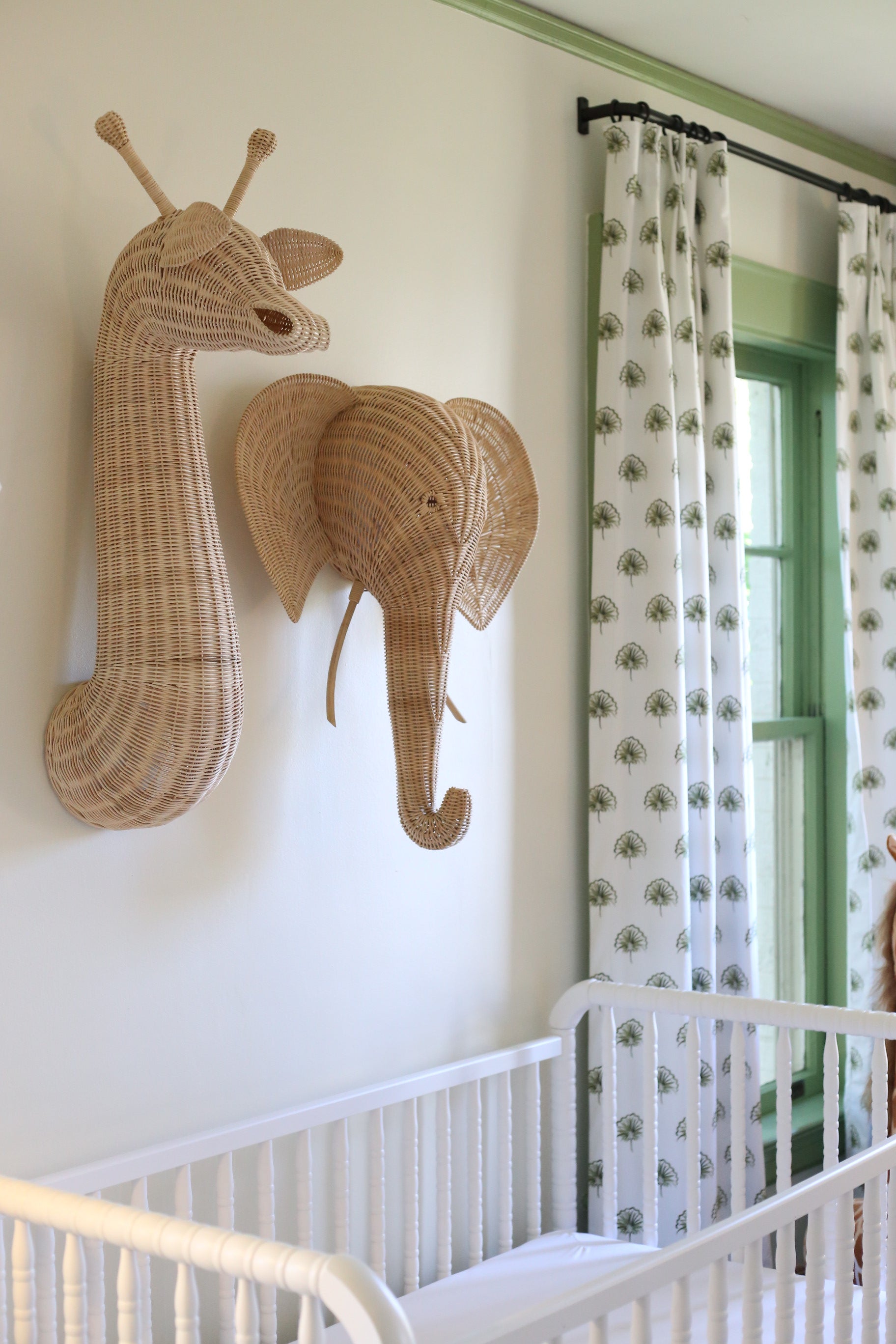 Hanging rattan elephant and giraffe next to green floral custom curtains hanging on a rod in front of a window and white crib