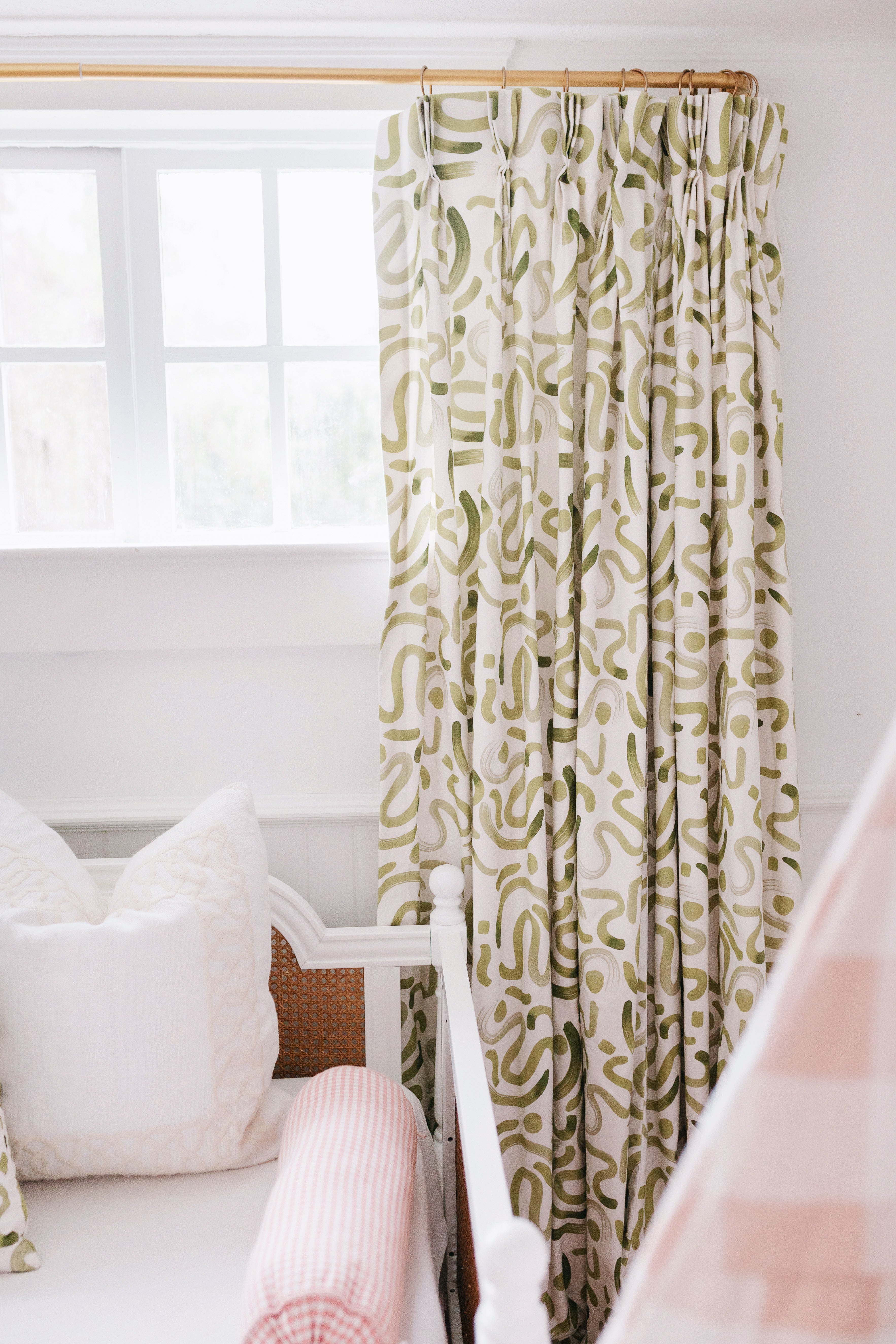 Close up of moss green abstract curtain panel hanging on a window in a playroom with a white daybed