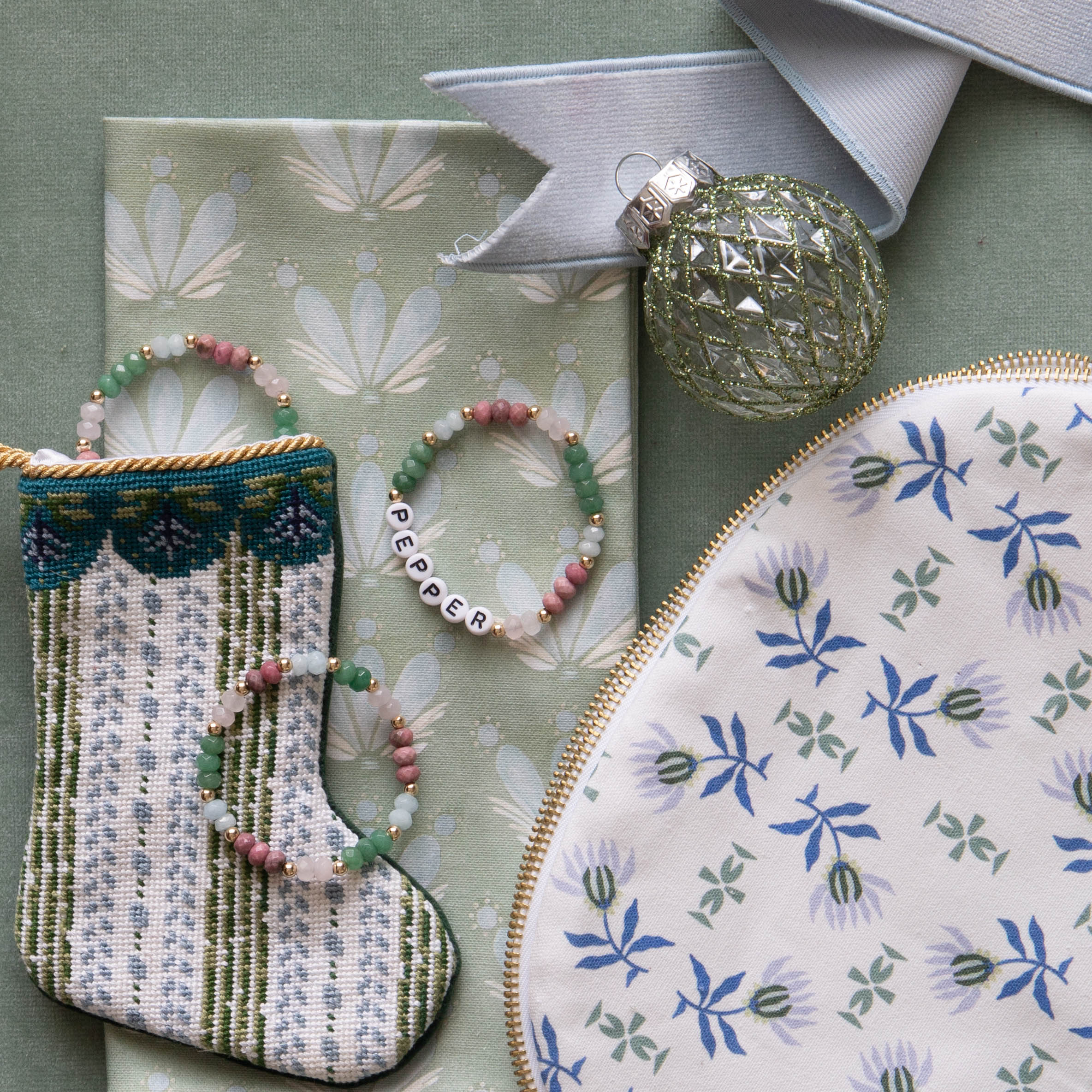 Blue and green floral drop repeat napkin styled with colorful beaded bracelet and blue and green striped stocking next to a blue and green patterned pouch