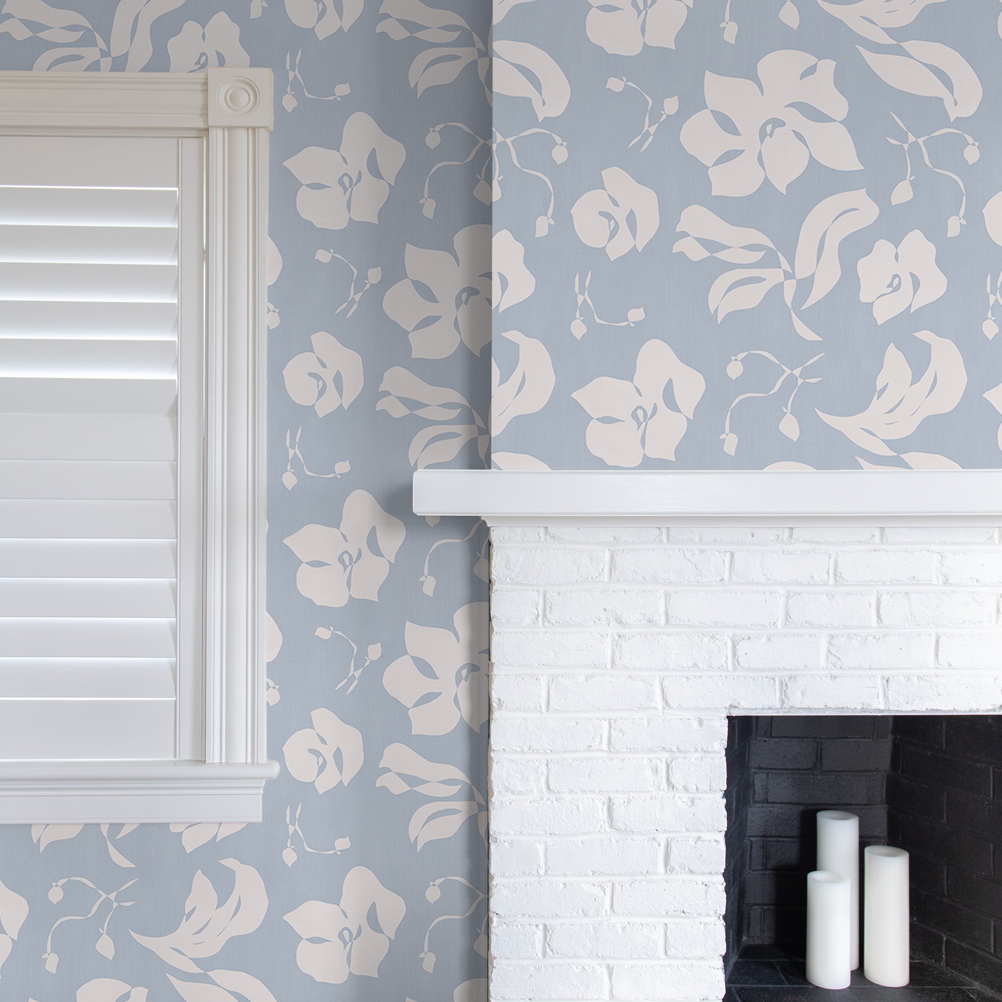 Close up of cornflower blue wallpaper in a room with a white fireplace and window with white shutters