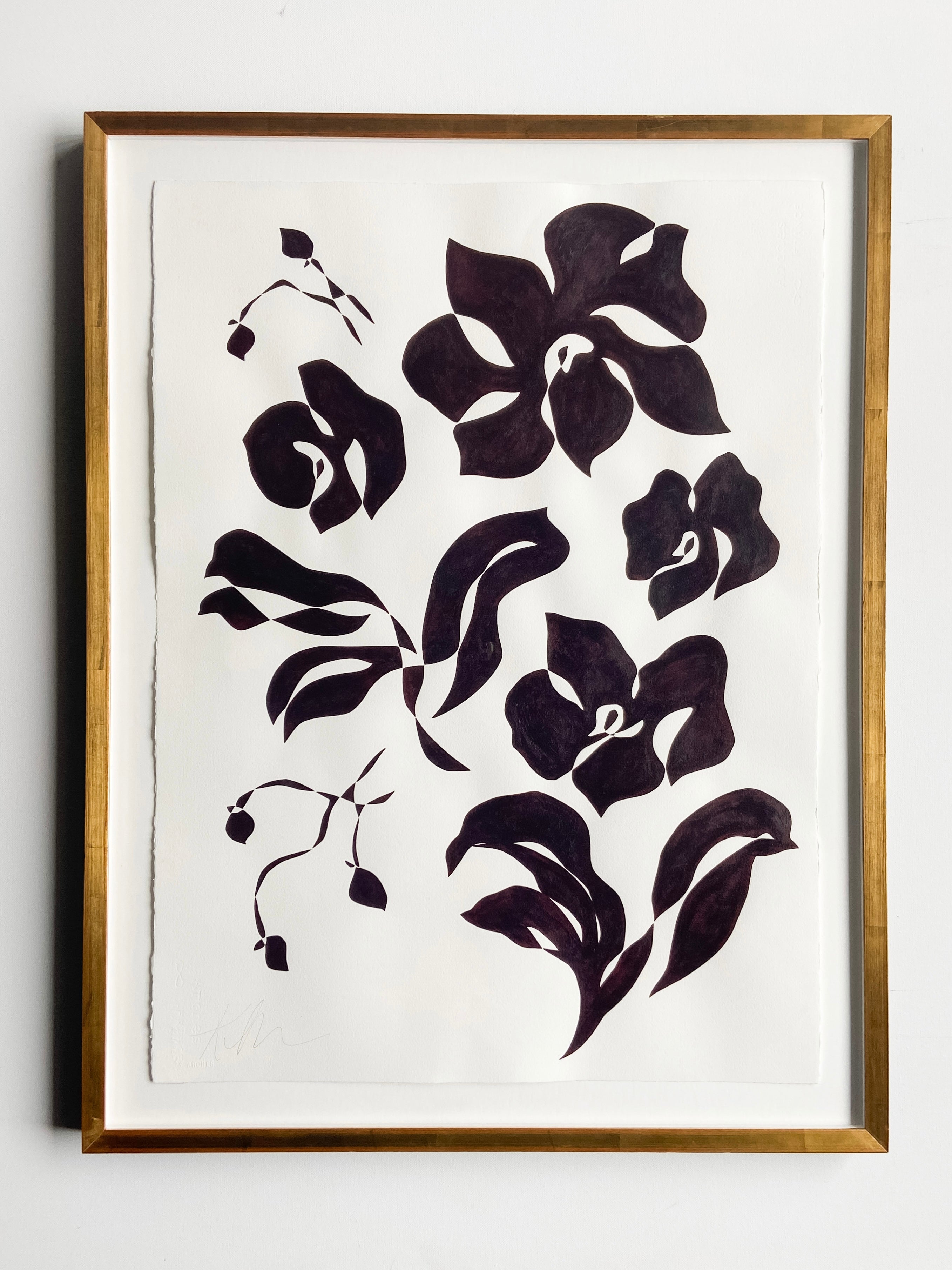 Black floral artwork in a gold frame on a white background