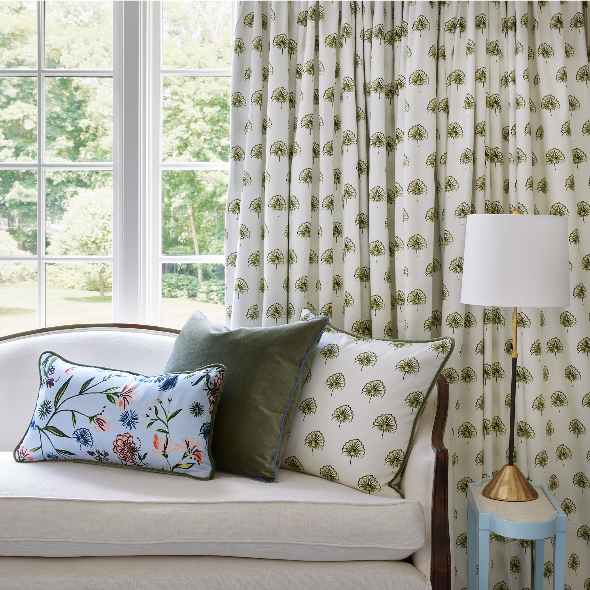 Green floral custom pillow, green velvet custom pillow, and blue chinoiserie custom pillow on a white bench in front of a window with green floral custom curtains