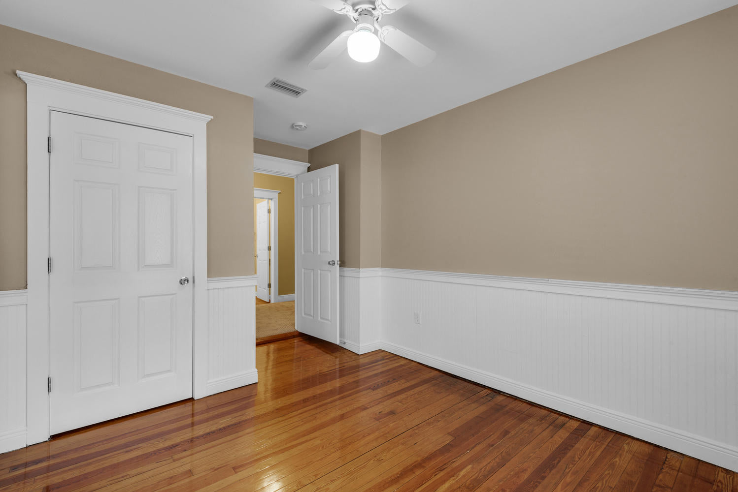 Empty room with wooden floors and tan walls with white wainscoting