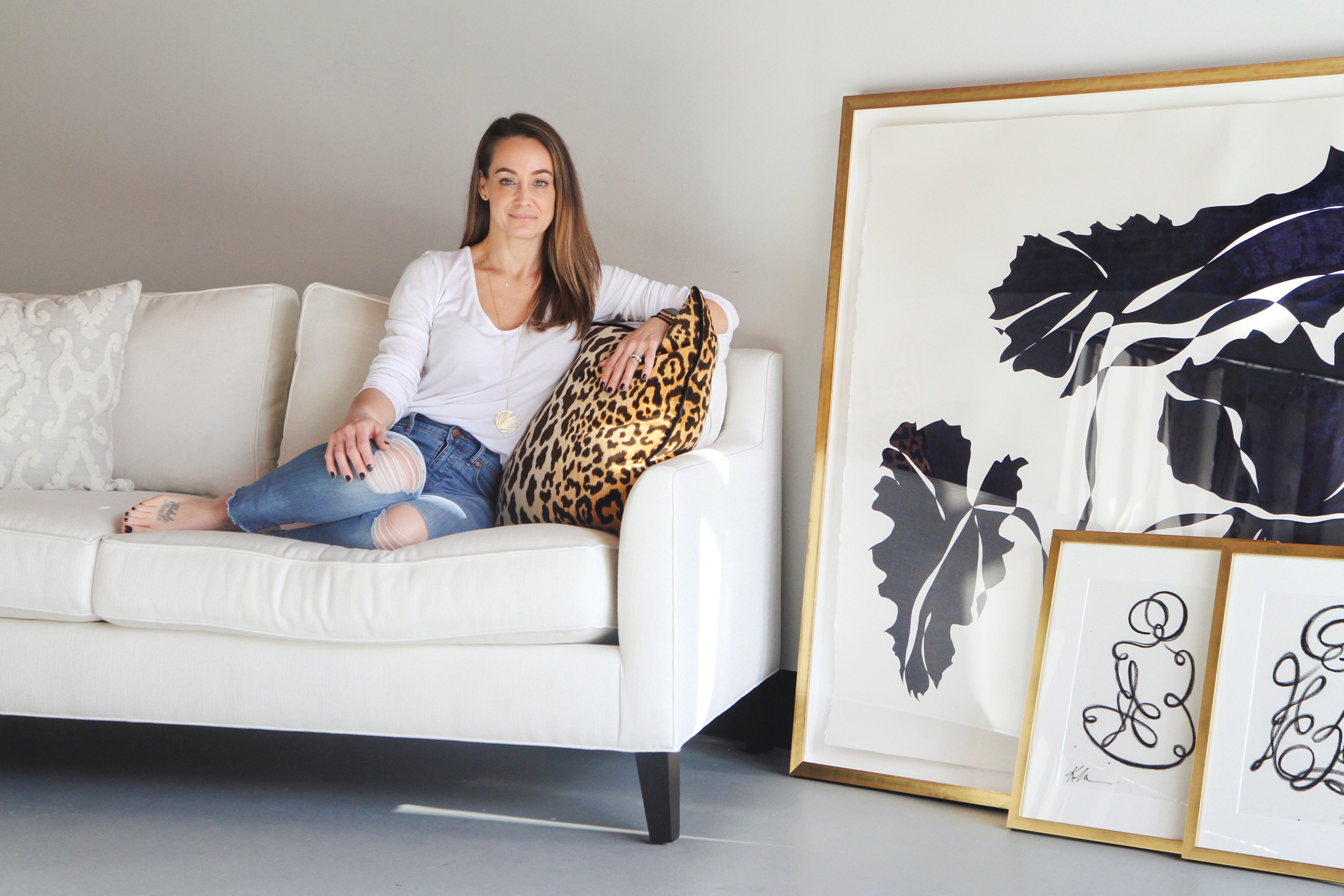 Brunette woman sitting on a white couch next to large pieces of modern artwork