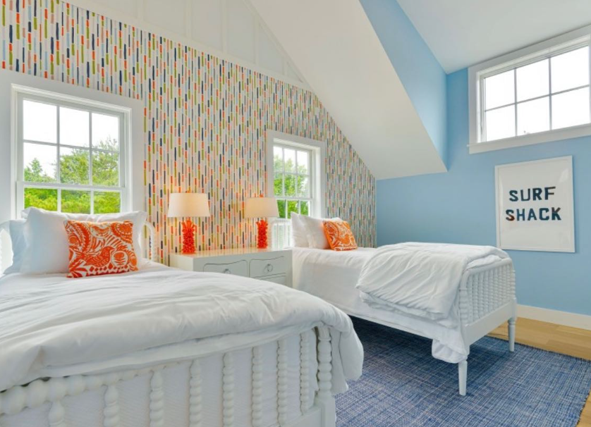 Colorful bamboo striped wallpaper on an accent wall in a bedroom with 2 windows and 2 white beds styled with white sheets