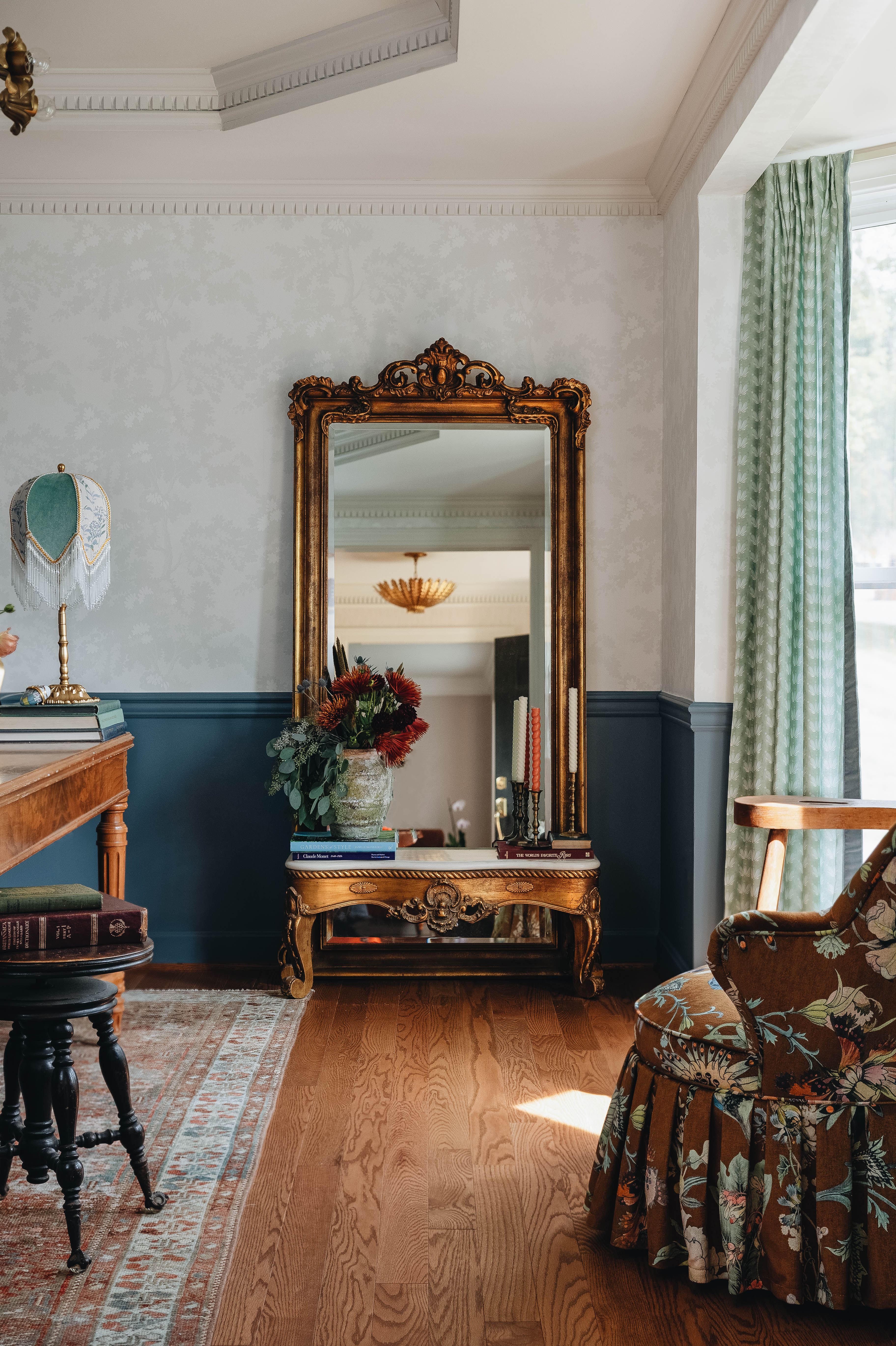 Large vintage mirror leaning on a wall in an office styled with coastal inspired green and blue curtains, white walls and blue painted wainscoting, and a wooden desk