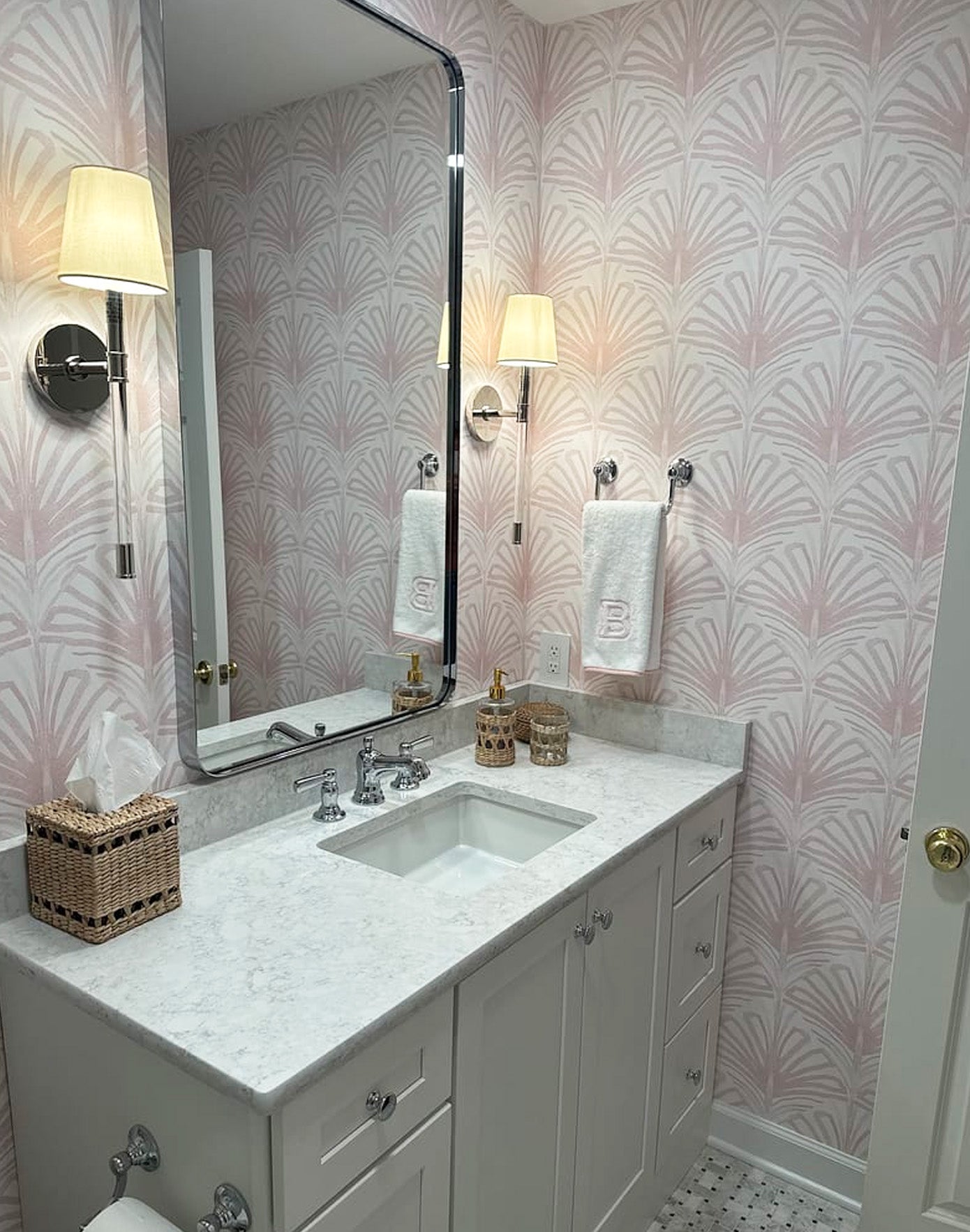 Powder bathroom with rose pink palm wallpaper and a white vanity with a silver mirror and sconces