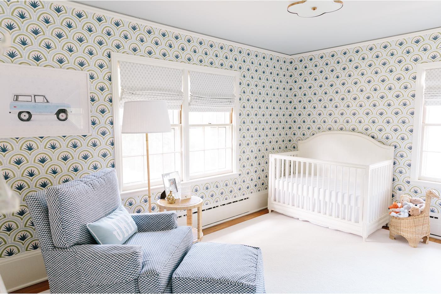 Nursery with green and blue art deco clay coated wallpaper, a white crib, and a blue and white patterned chair