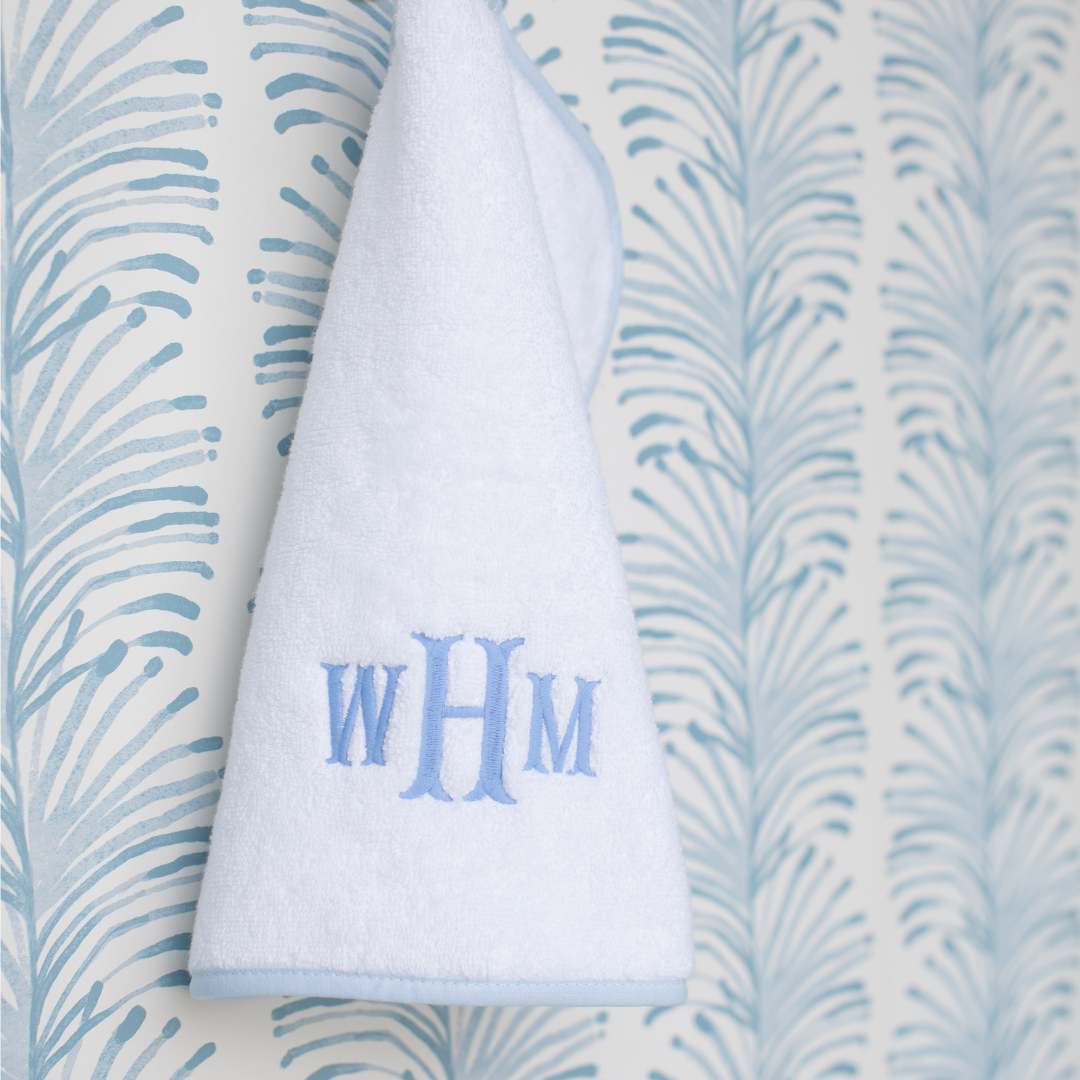 close up of white handtowel with blue WHM monogram hanging on sky blue botanical wallpaper