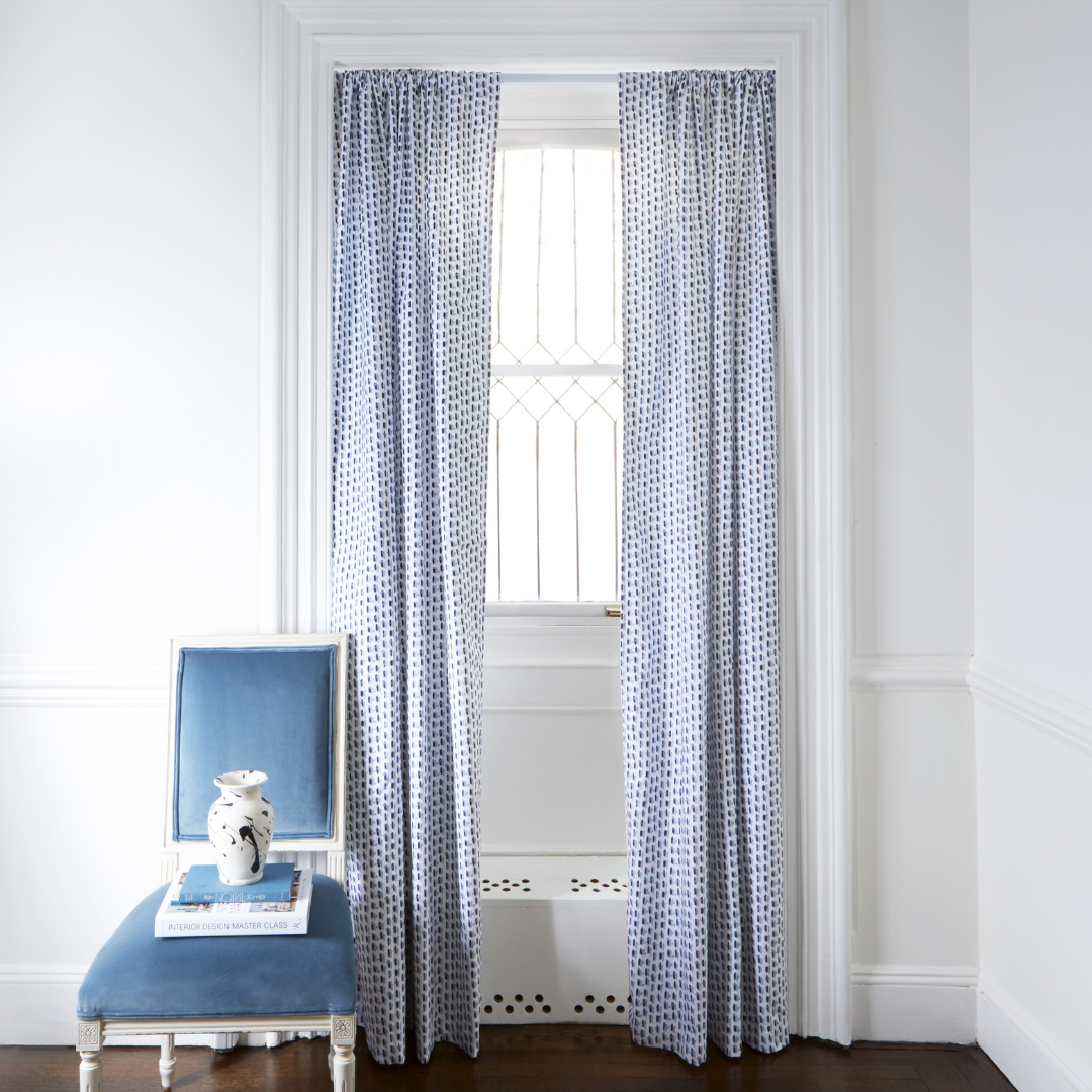 Blue patterned custom curtain hanging on window in room with white walls and blue chair