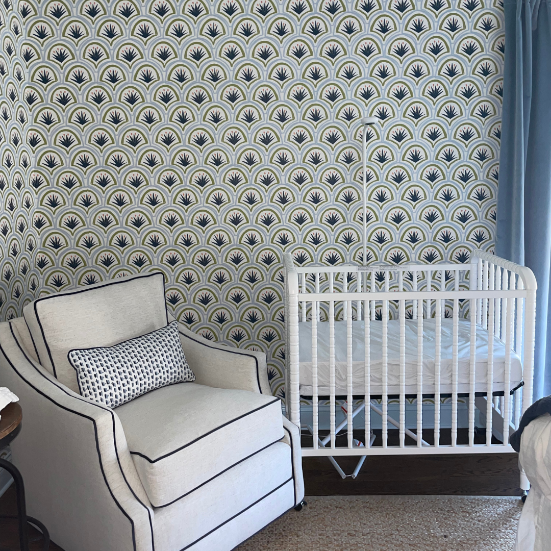 Bedroom with blue and green art deco palm wallpaper styled with a white crib and white glider with a blue patterned custom pillow