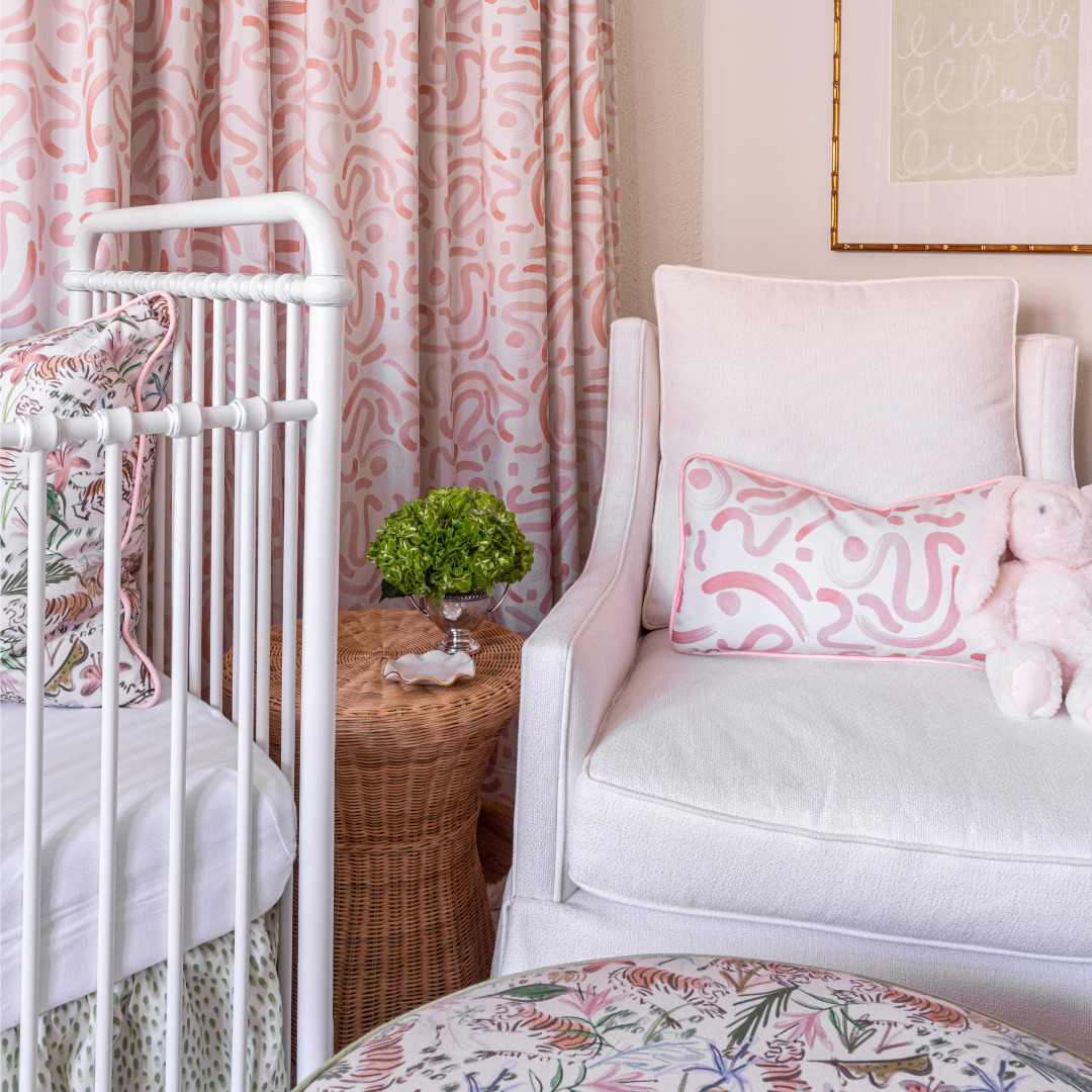 Nursery room corner styled with Pink Graphic Custom Lumbar on Pink Sofa Chair next to white crib with Pink Chinoiserie Custom Pillow and Pink Graphic Custom Curtains