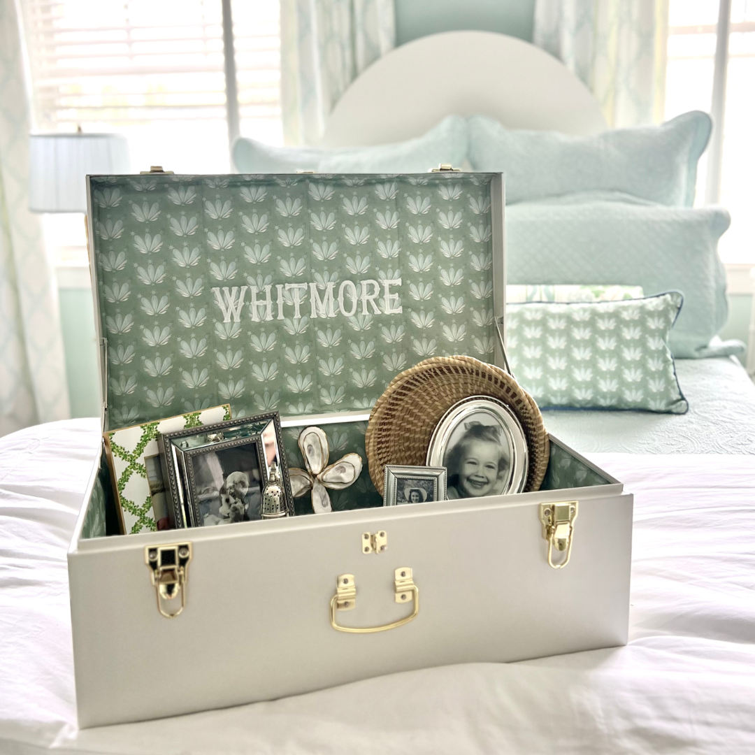 White drunk with blue and green floral fabric on the inside filled with black and white photographs and a rattan basket