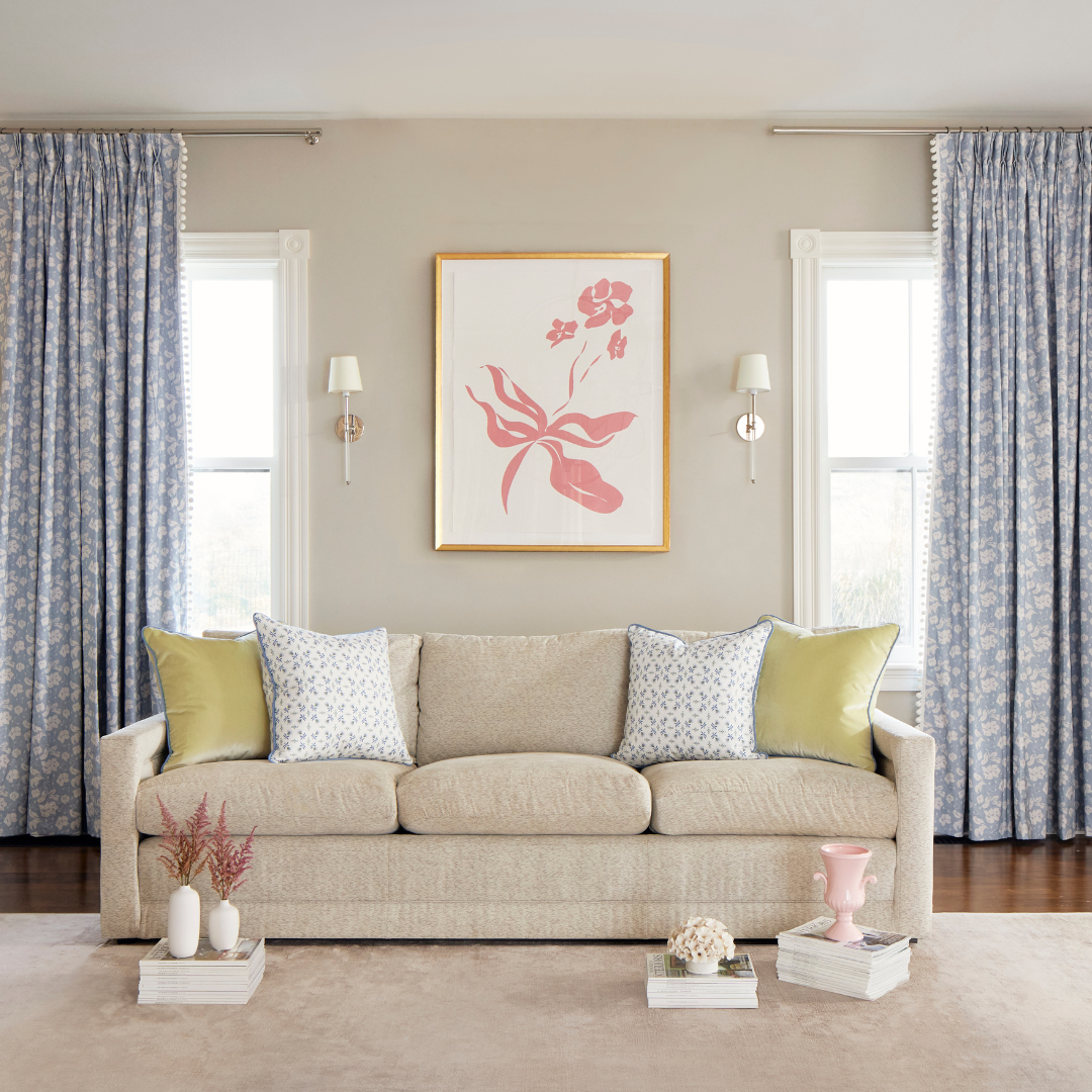 Cornflower blue custom curtains hanging on a rod in a grey painted living room next to pink floral artwork and a beige couch with light green pillows and blue and green floral custom pillows