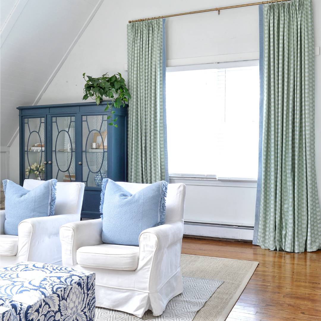 Illuminated window styled with Coastal Inspired Green and Blue custom curtains next to two blue sofa chairs with one blue pillow on each