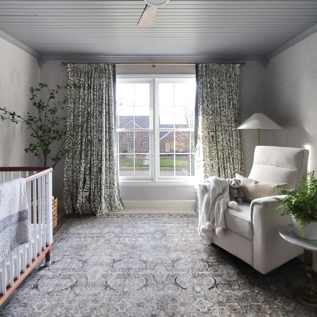 Nursery room with crib by plant and white sofa chair next to window styled with Moss Green custom curtains
