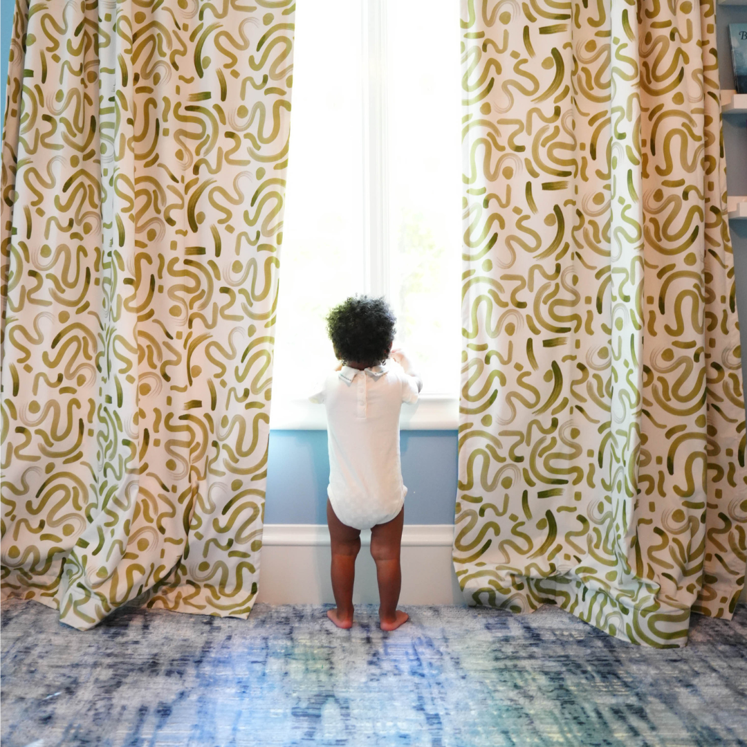 Baby standing in between Moss Green Custom Curtains in front of an illuminated window