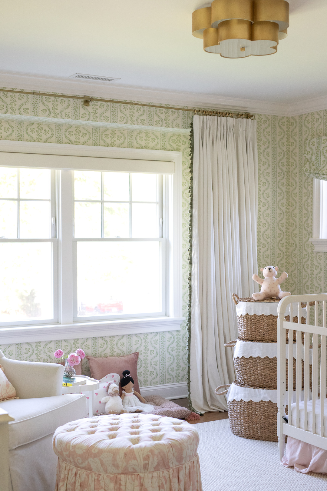 Nursery with green wallpaper and a natural white curtain with sage tassel trim complimented with rattan baskets