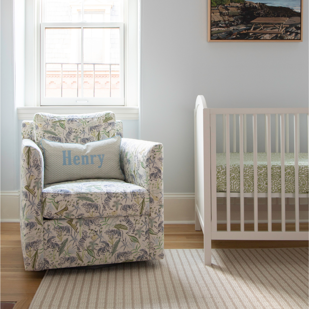 green tiger chair with a moss green geometric patterned pillow embroidered with "Henry" next to a white crib