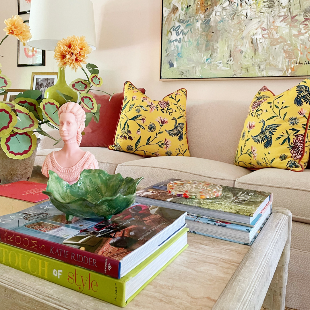 Living room styled with a white couch with a coral velvet custom pillow and two yellow chinoiserie custom pillows next to a coffee table with decorations and a plant