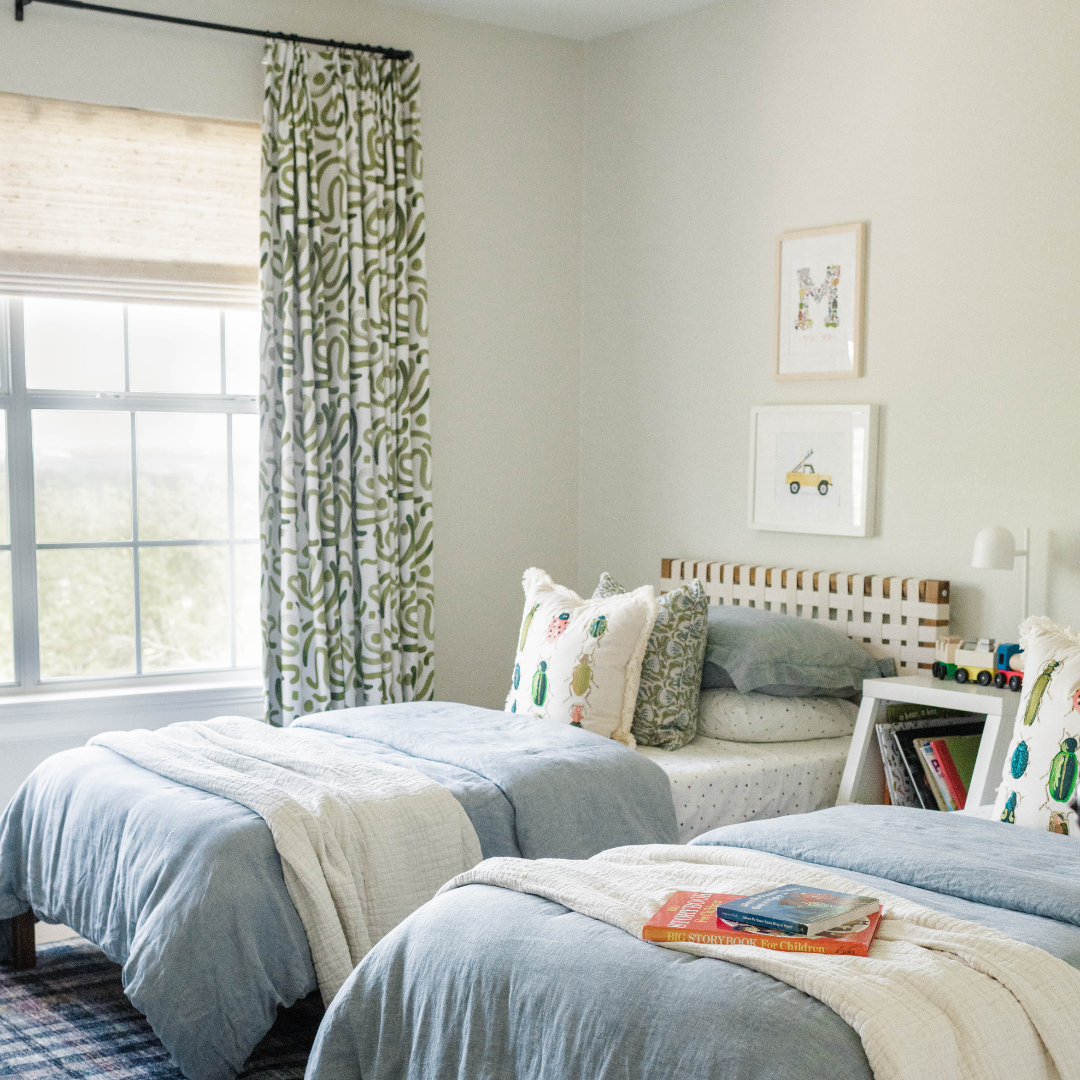 Kids bedroom with an abstract moss green curtain panel hanging on a window next to two twin beds with blue, white and green bedding