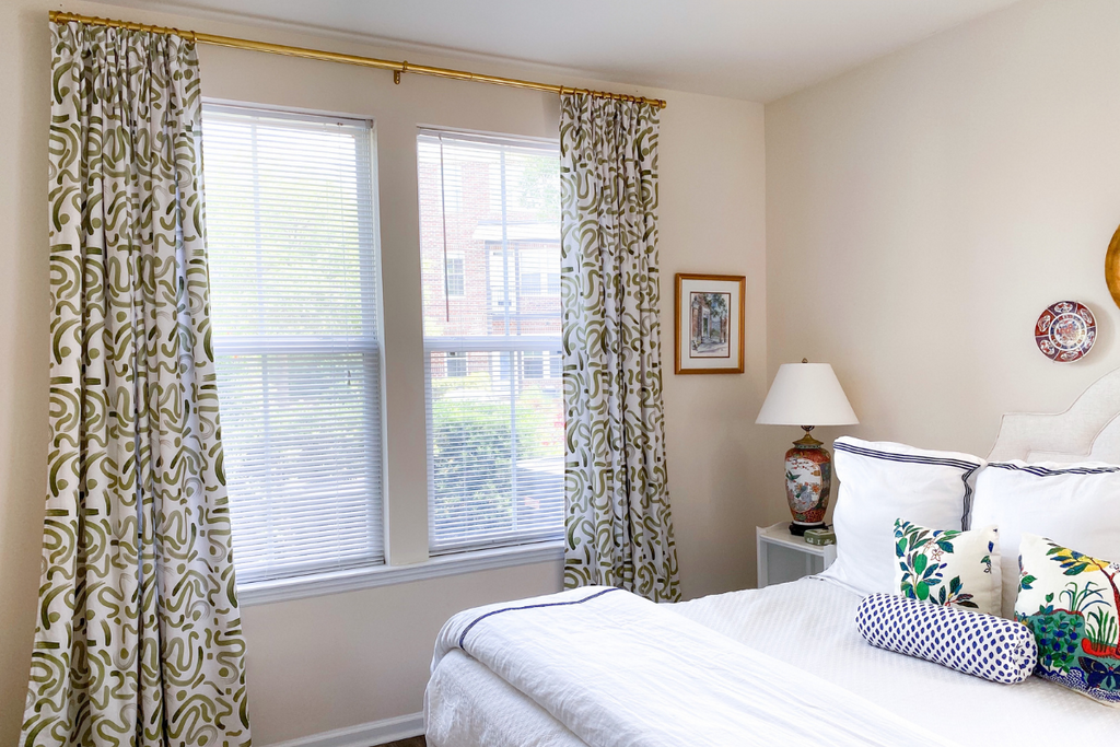 Custom moss green curtains hanging on a gold rod in front of a window in a bedroom with a white bed and sheets