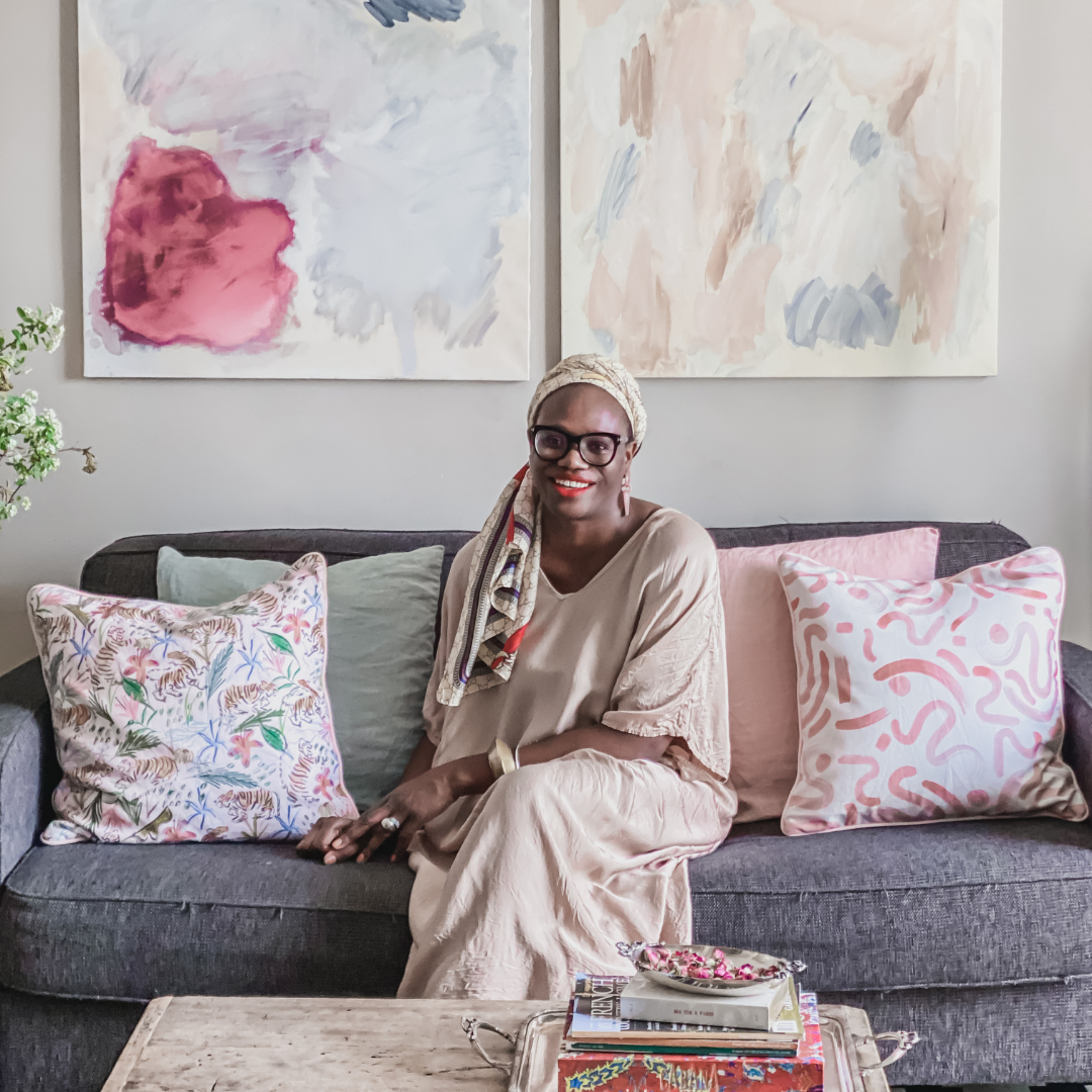 Woman sitting on grey couch in between a Pink Chinoiserie Tiger custom pillow, a green pillow, a pink pillow, and a Pink Graphic custom pillow in front of a coffee table