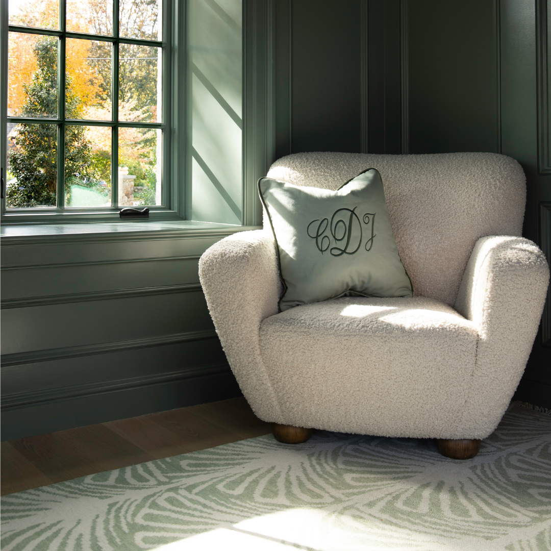 Sage green pillow embroidered with CDJ on a white boucle chair in a green room