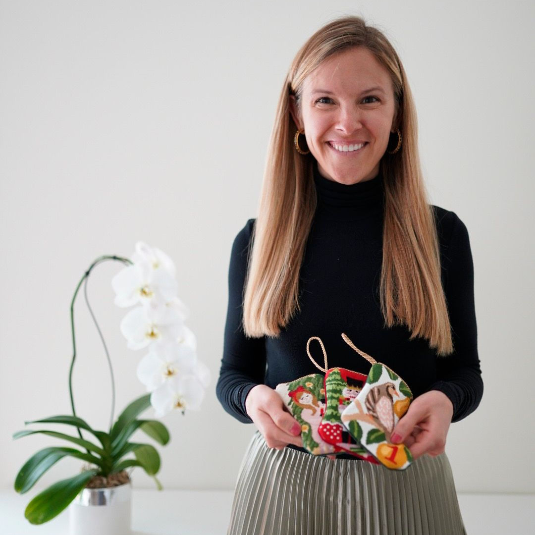 Blonde woman holding three mini stockings in a white room next to a white orchid