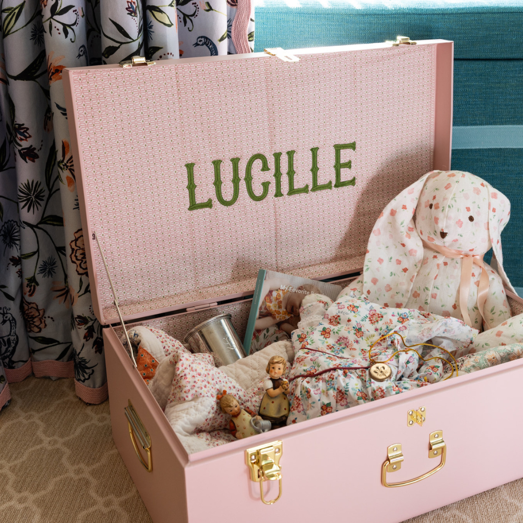 Pink keepsake trunk with pink and green fabric on the inside stuffed with childrens keepsakes and stuffed animals