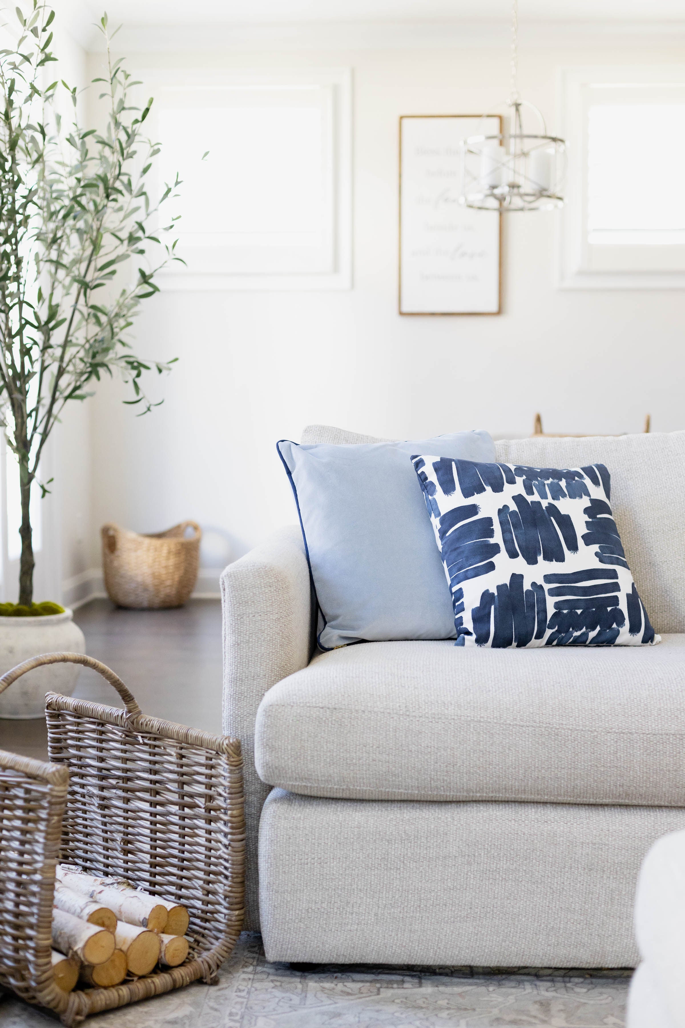 Navy Brushstokes Pattern pillow styled with a sky velvet pillow on a white couch next to wooden logs in a rattan basket