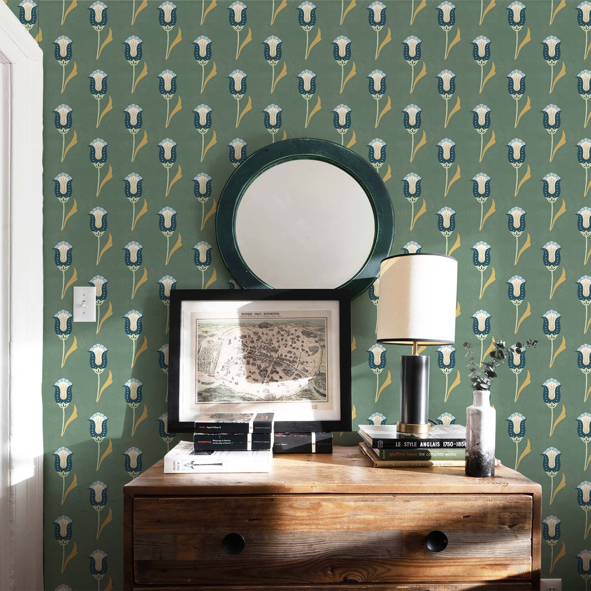 Vignette of a room with Green, navy and blue tulip wallpaper styled with a wooden dresser and green round mirror