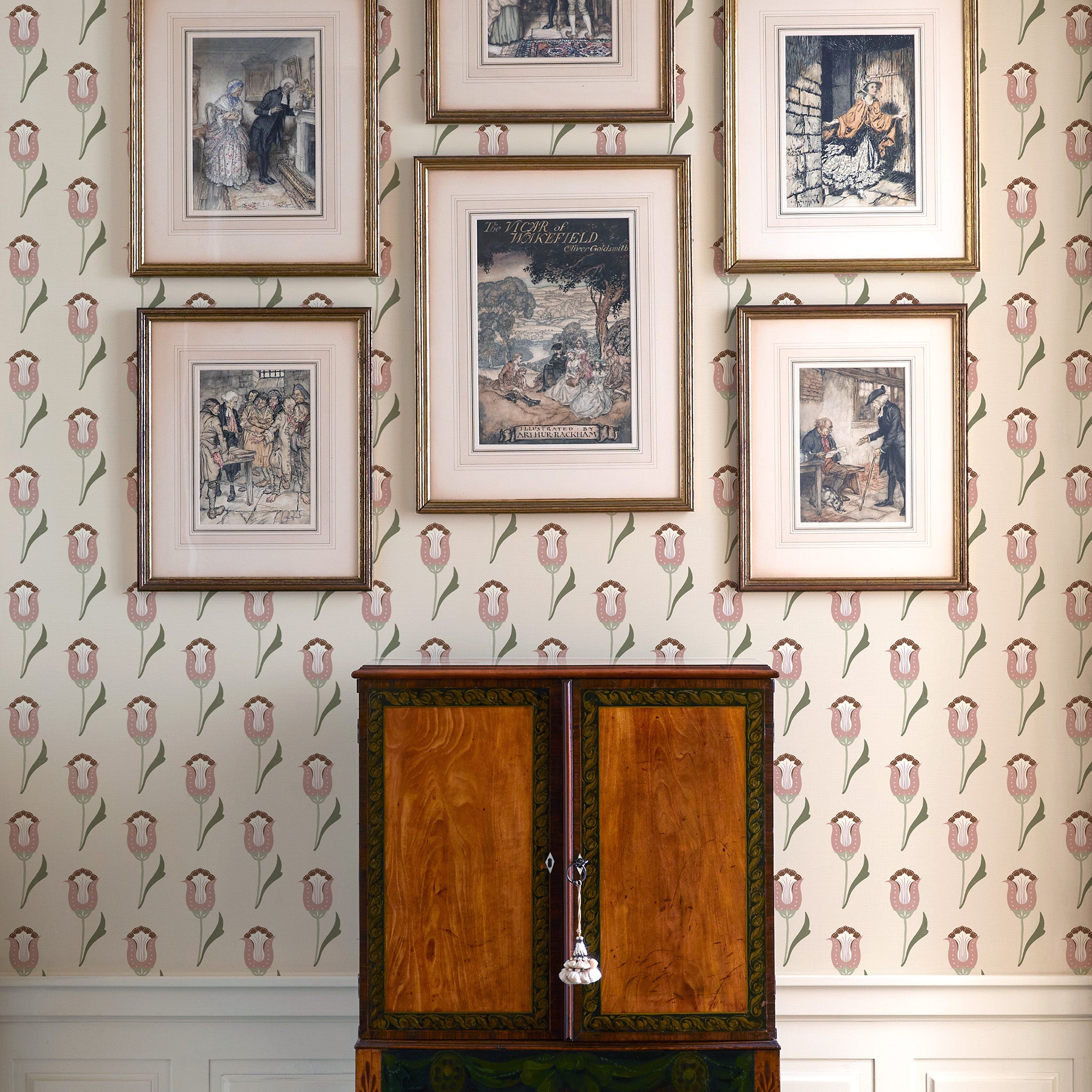 Light pink and green floral drop repeat clay coated wallpaper on a wall behind a wooden chest styled with a gallery wall