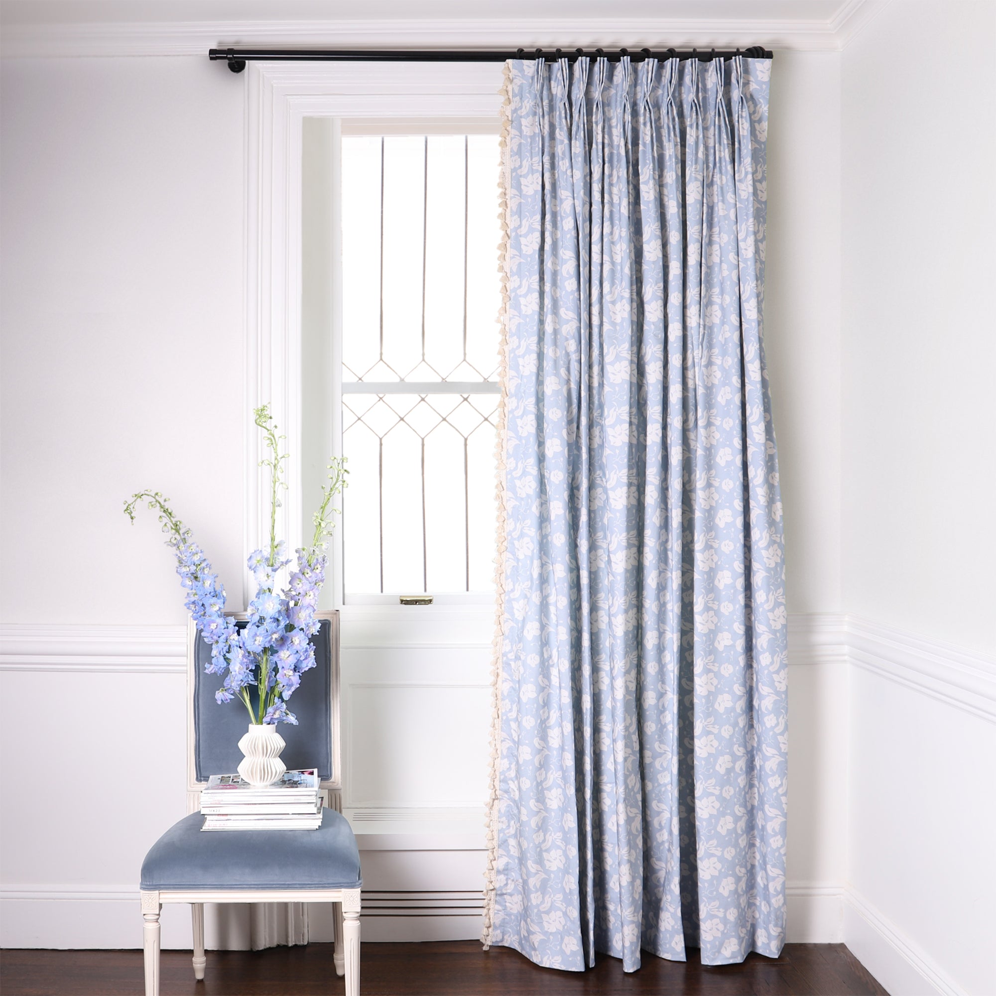 Cornflower blue floral custom curtain hanging on window in room with white walls and blue chair