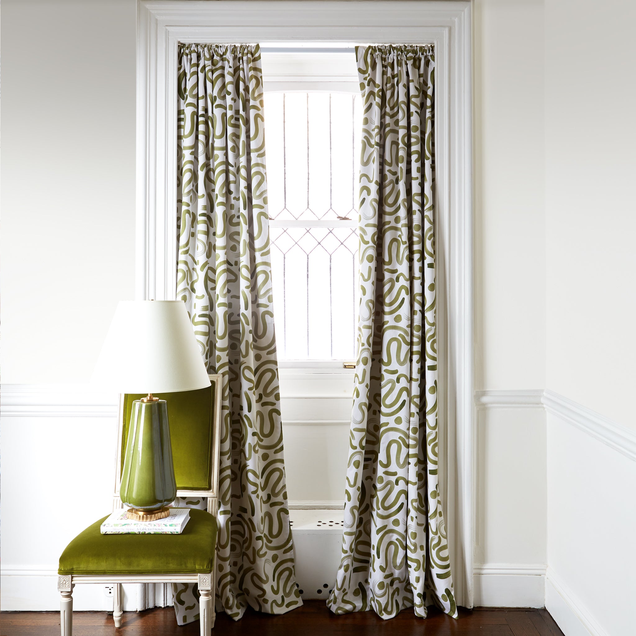 Green abstract custom curtain hanging on window in room with white walls and green chair