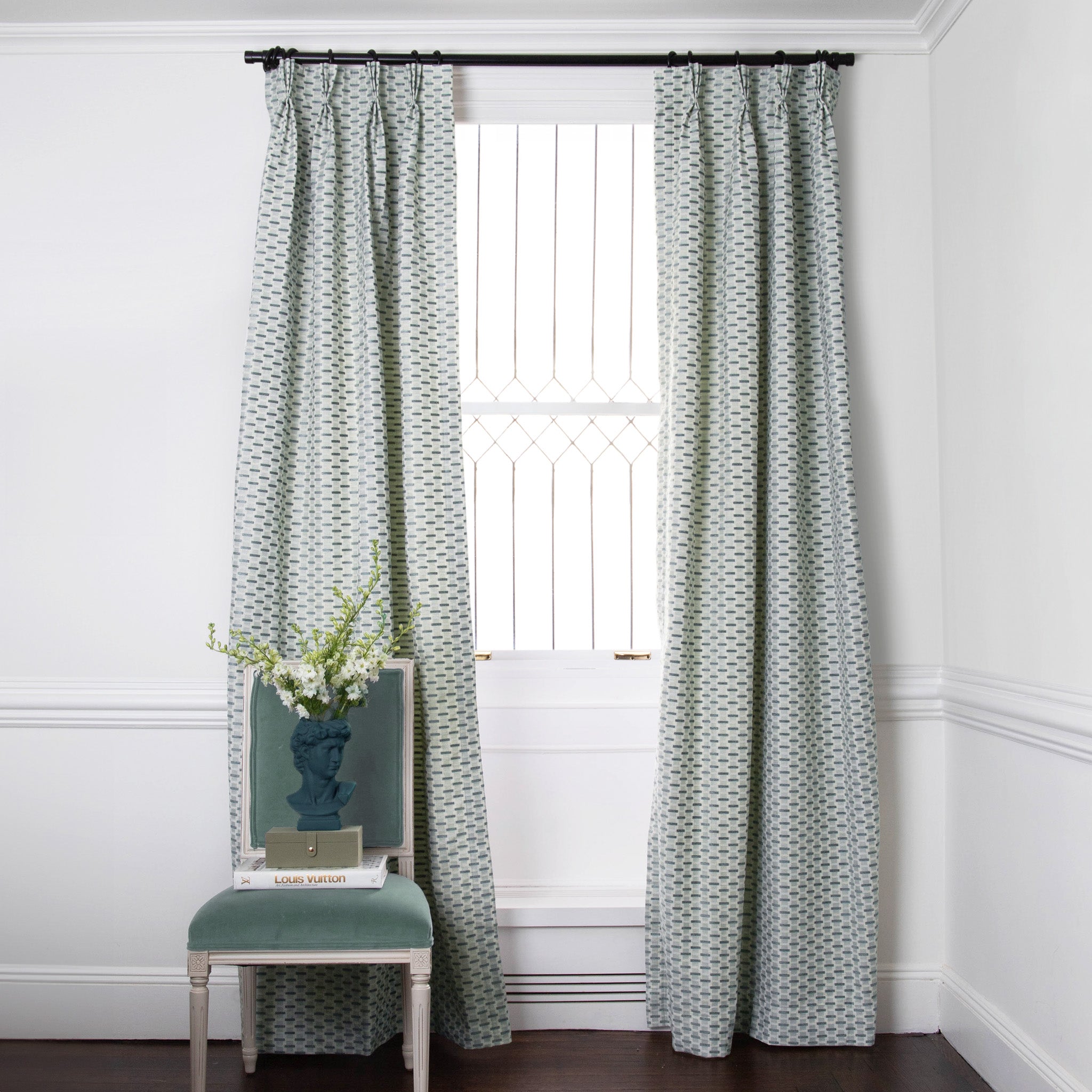 Green chenille and woven jacquard custom curtain hanging on window in room with white walls and green chair