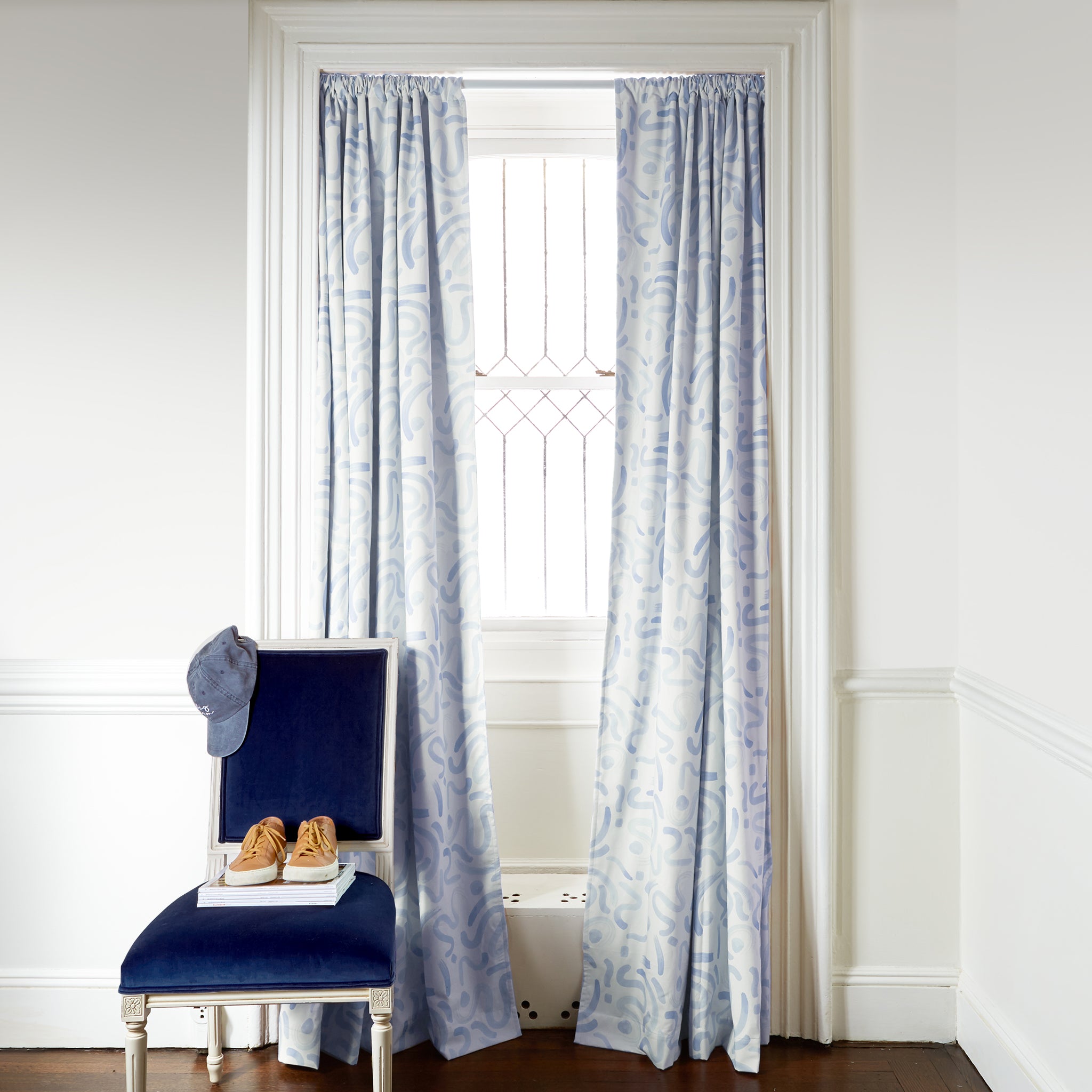 Sky blue abstract custom curtain hanging on window in room with white walls and navy chair