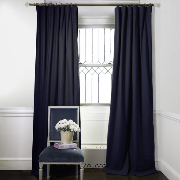 Navy Blue Custom Curtains  on metal rod in front of an illuminated window with a Navy Blue Velvet chair with a book and white flowers in vase on top