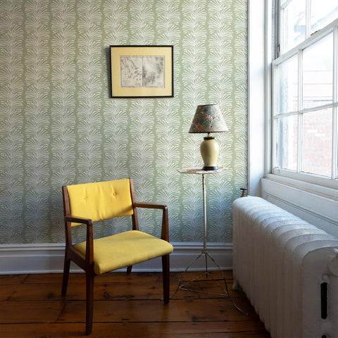 Nursery Room corner styled with Sage Botanical Stripe custom wallpaper with wooden yellow chair in front by green and floral lamp on white circular small table next to window
