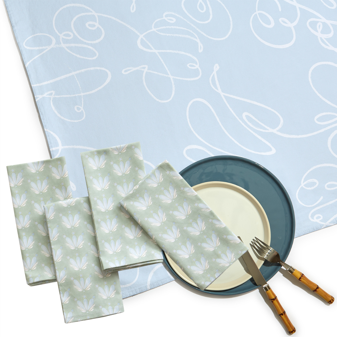 Powder Blue Abstract Custom Table Linen with four folded Blue & Green Floral Drop Repeat custom napkins, two plates, and silverware