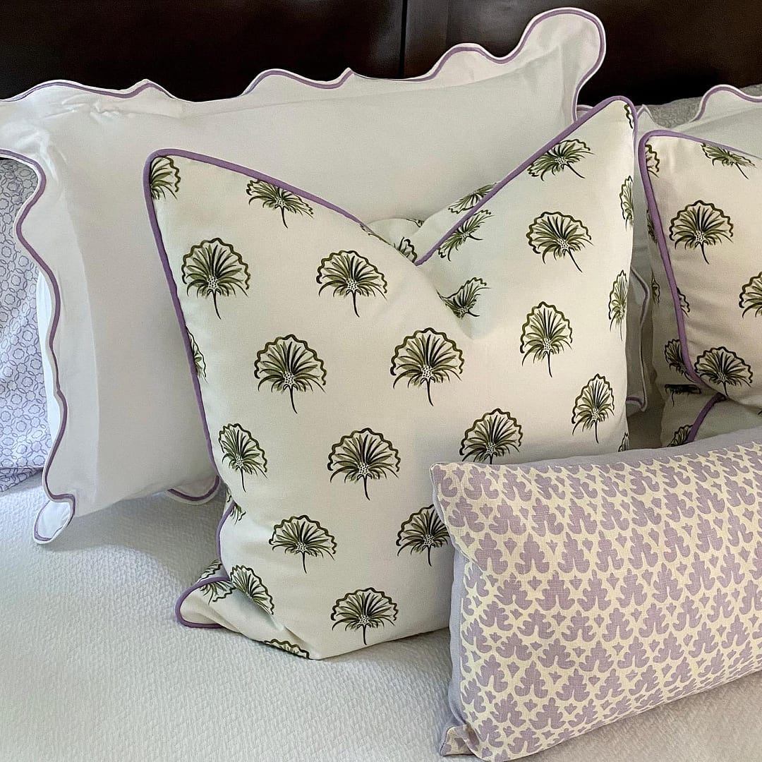 Green floral custom pillows with lilac piping styled on a bed with purple geometic pillows and white pillows