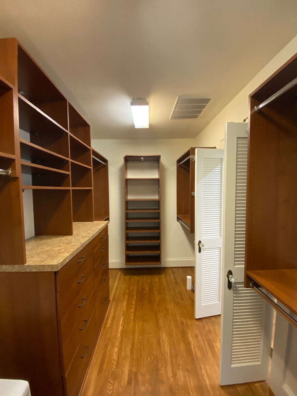 Narrow walk in closet with brown shelves and drawers and white painted walls