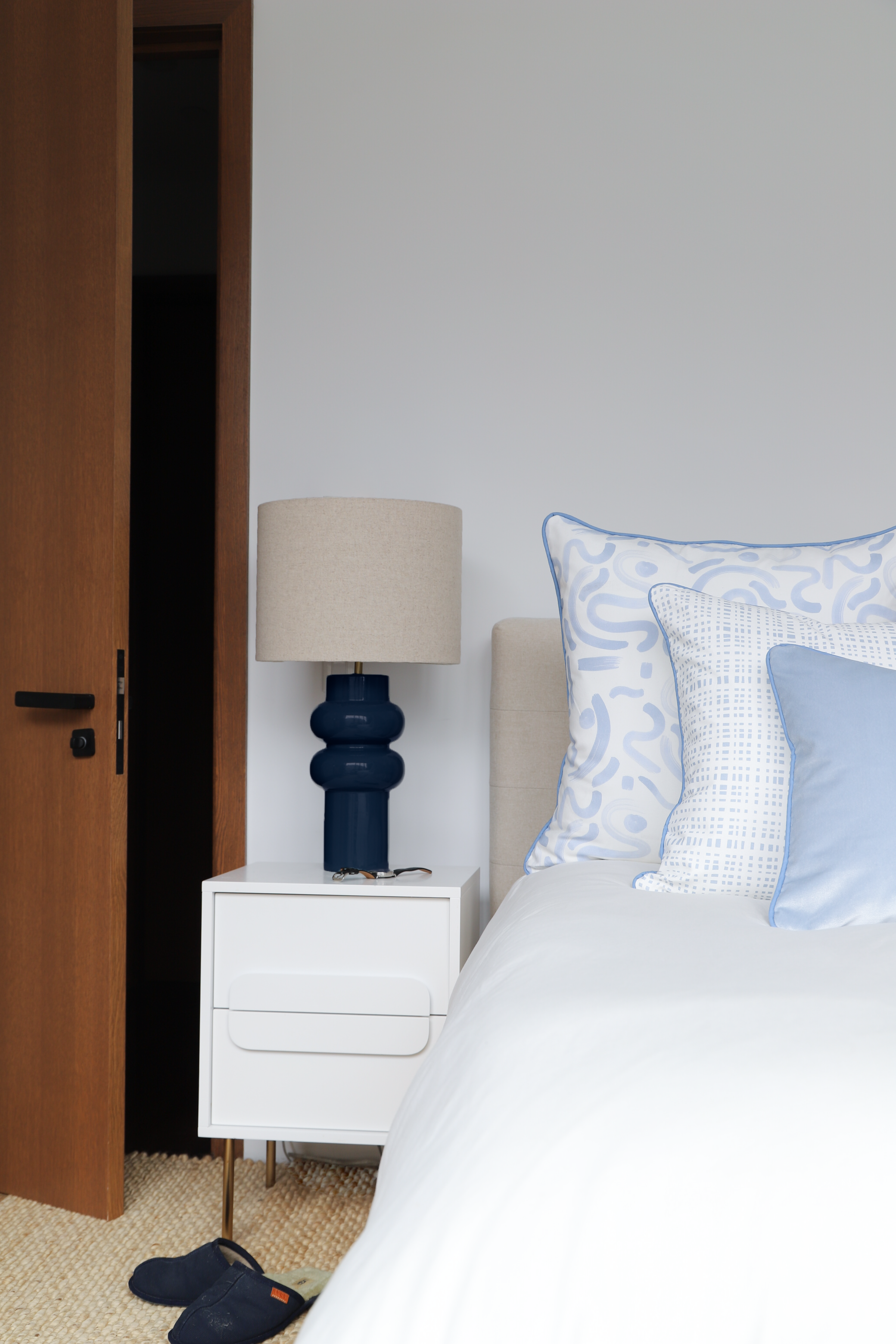 White modern bedroom with beige headboard with blue abstract pillow, blue gingham pillow and blue velvet pillow