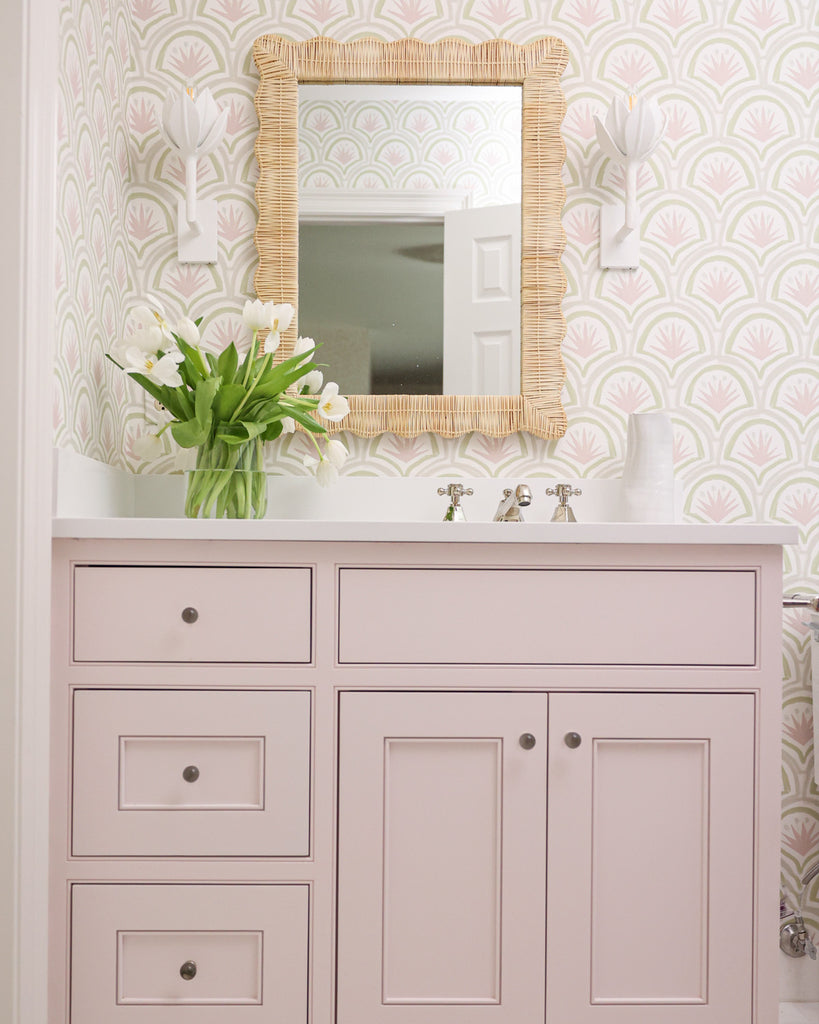 Bathroom sink styled with pink cabinets and a Pink & Green Palm custom wallpaper with a mirror in the center