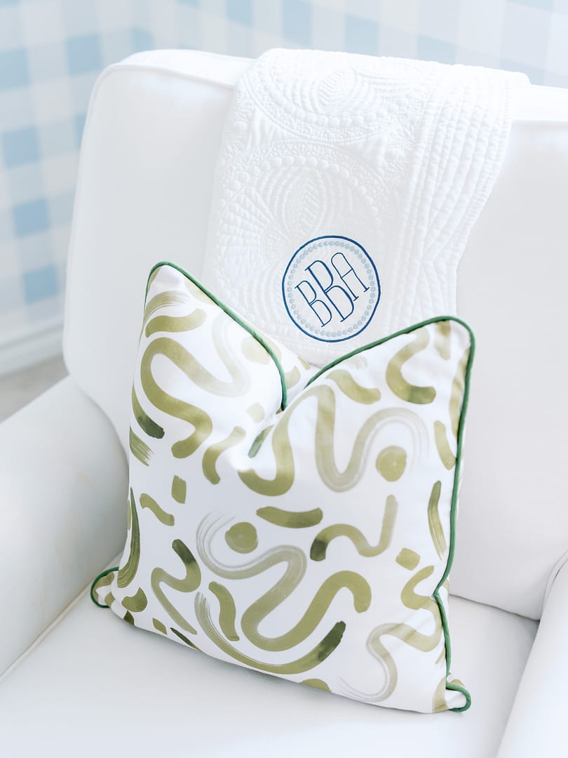Moss green custom pillow with moss piping on a white chair in a nursery with blue gingham wallpaper